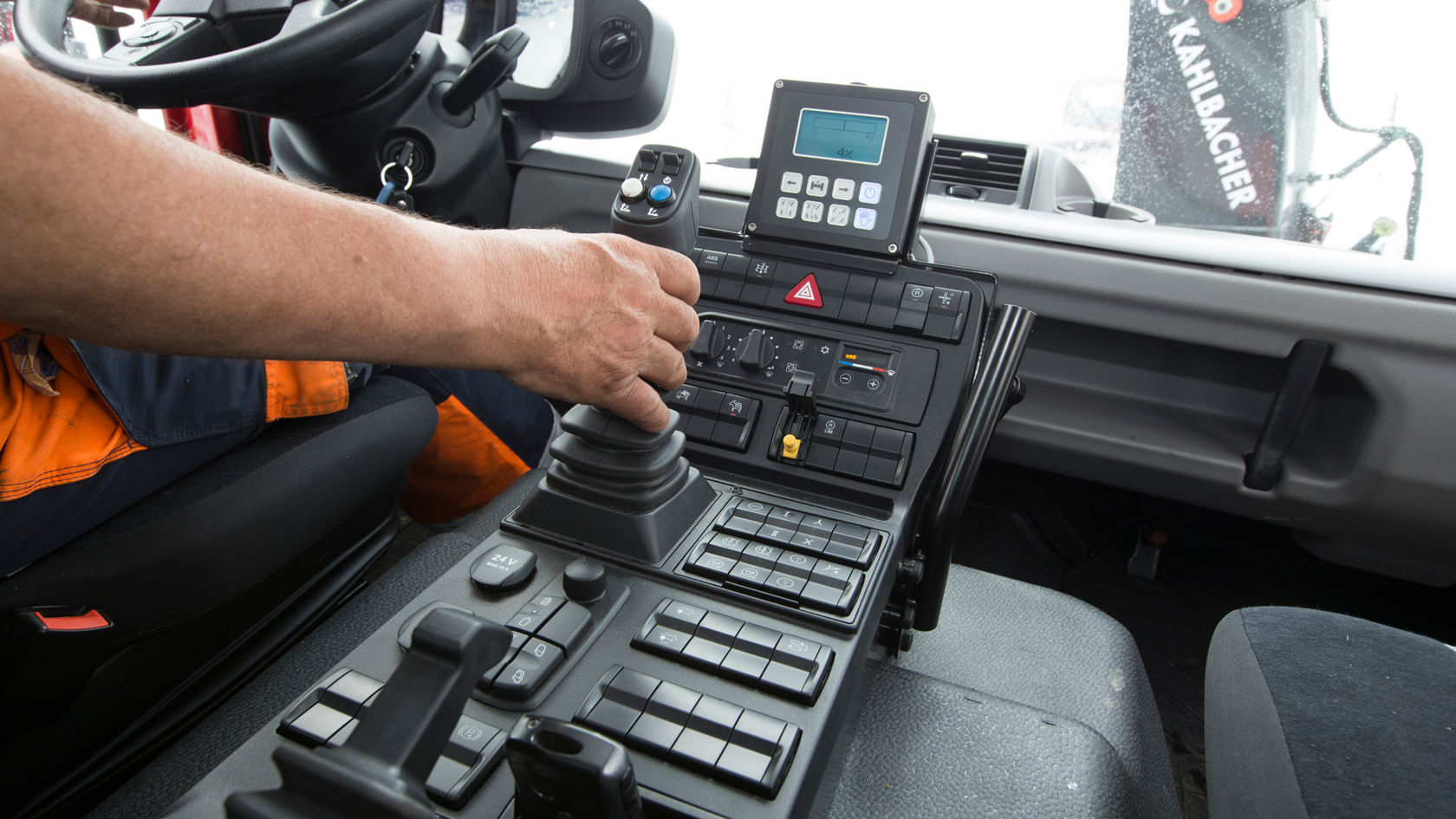 Le conducteur d'un Unimog Mercedes‑Benz utilise la console de commande, dotée de divers éléments et boutons, tandis qu'un écran numérique est bien visible.