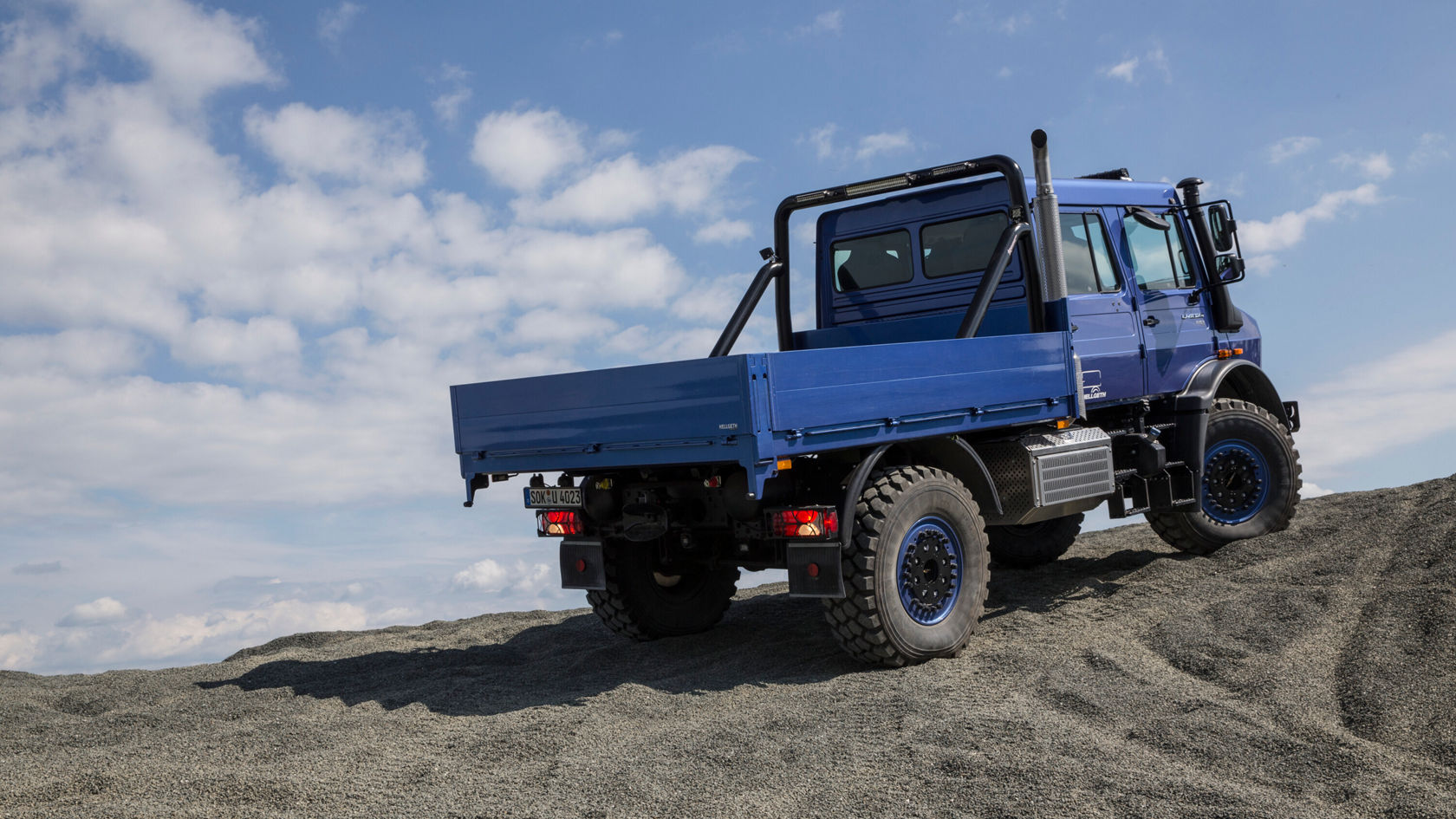 Ein blauer Unimog U 4023 mit Pritsche steht auf einem Schotterhügel. 