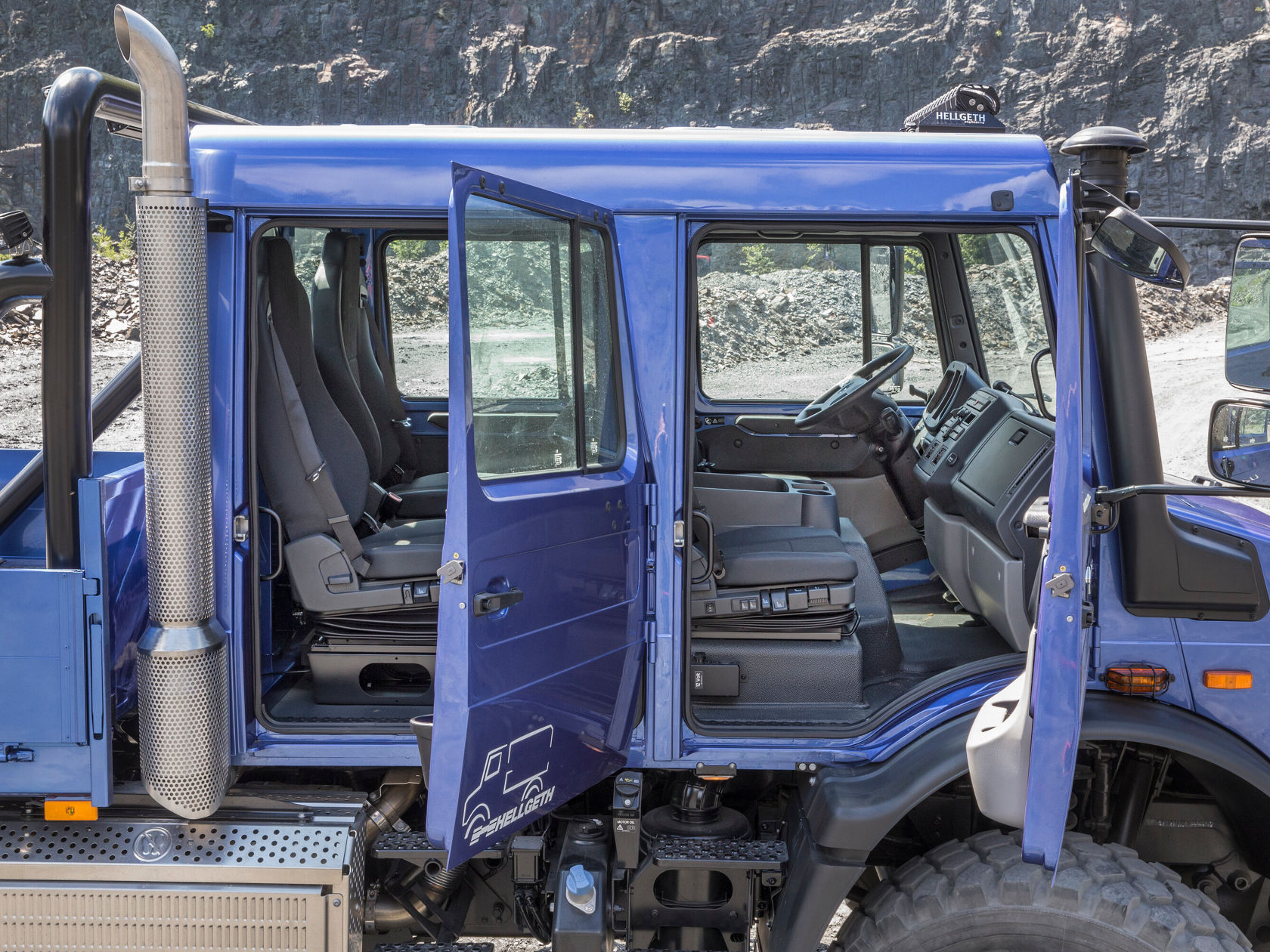 Ein Unimog U 5023 mit Doppelkabine steht in einer Steinbruchumgebung. Die Türen sind offen und zeigen den Innenraum.
