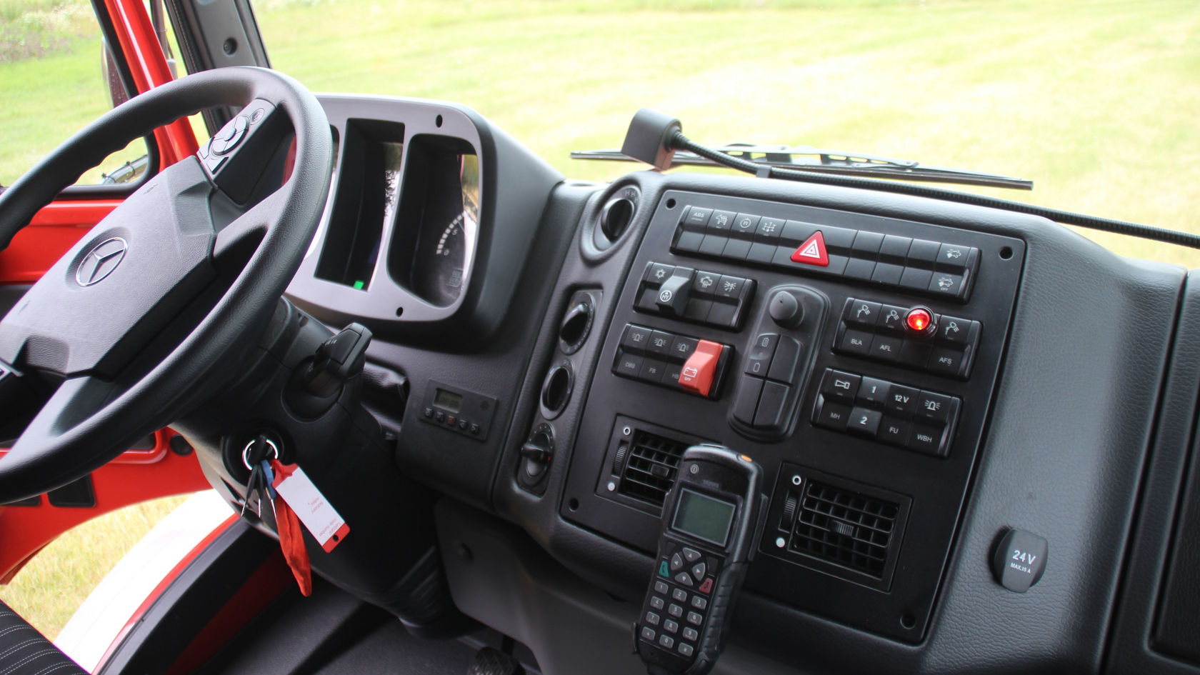 Das Armaturenbrett eines Mercedes-Benz Trucks zeigt das Lenkrad, zahlreiche Bedienelemente, Schalter und Displays. Das Design ist funktional und auf Fahrzeugbetrieb ausgerichtet.