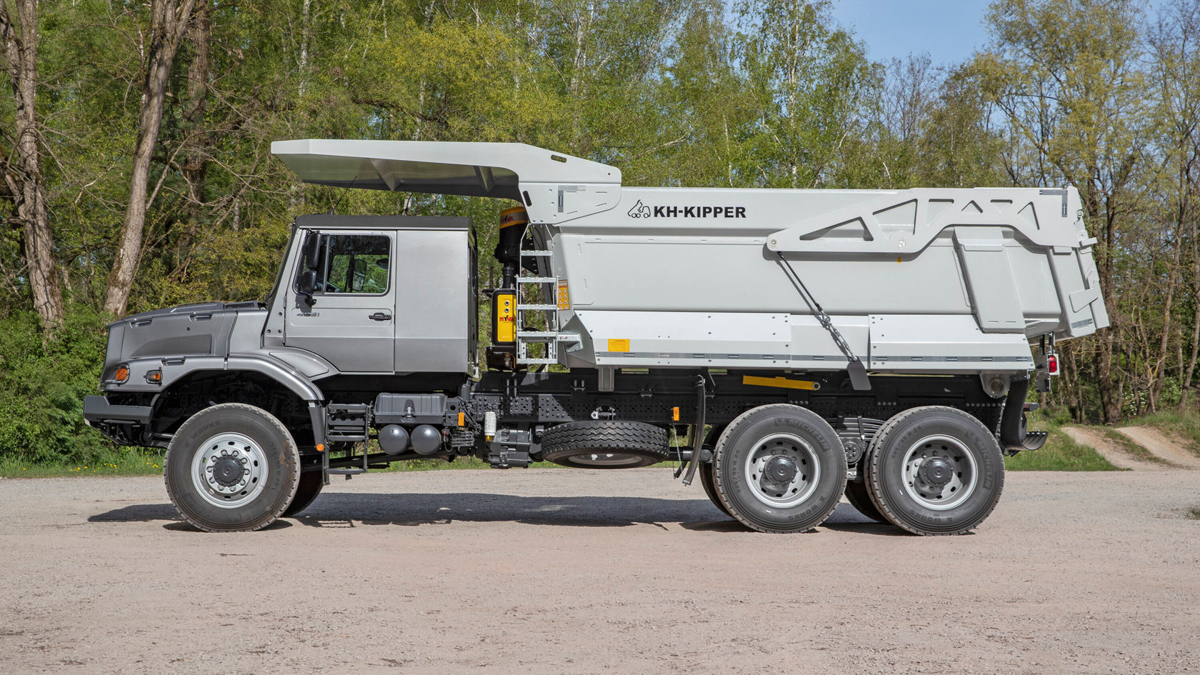 Ein Mercedes-Benz Kipper-Lkw steht auf einer Baustelle. Er ist mit einer großen, grauen Ladeschaufel ausgestattet und hat ein robustes, geländetaugliches Design.