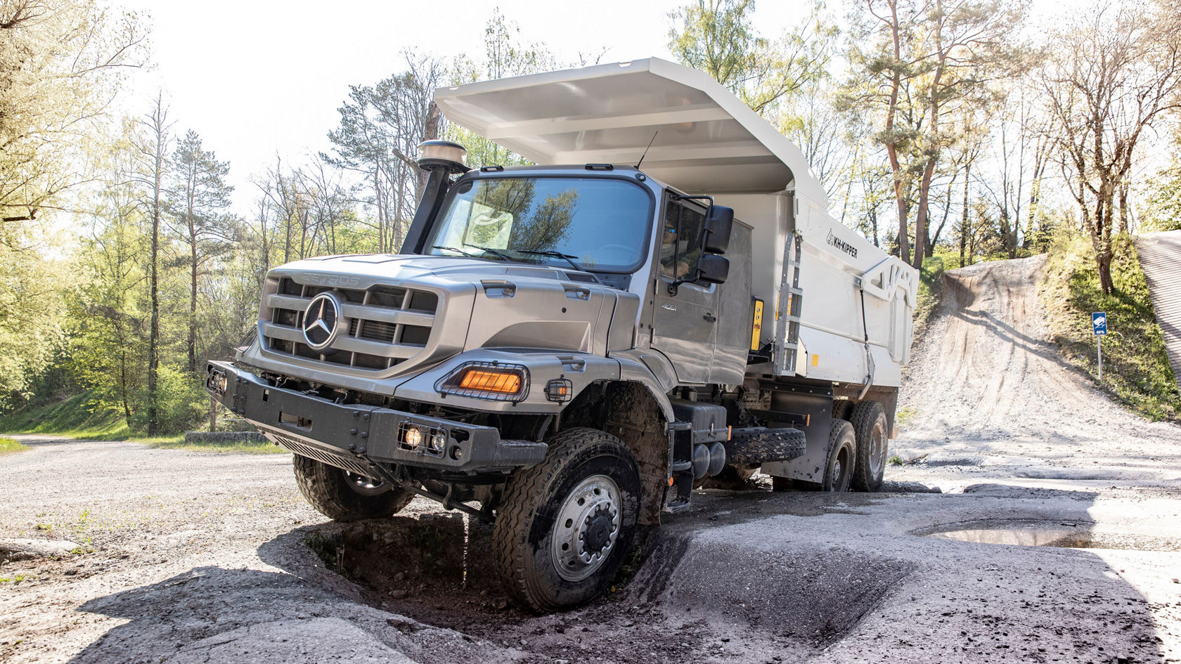 Ein Mercedes-Benz Lkw steht auf unbefestigtem Gelände mit einer offenen Ladefläche. Das Fahrzeug zeigt robuste Eigenschaften und ist für anspruchsvolle Transportaufgaben ausgelegt.