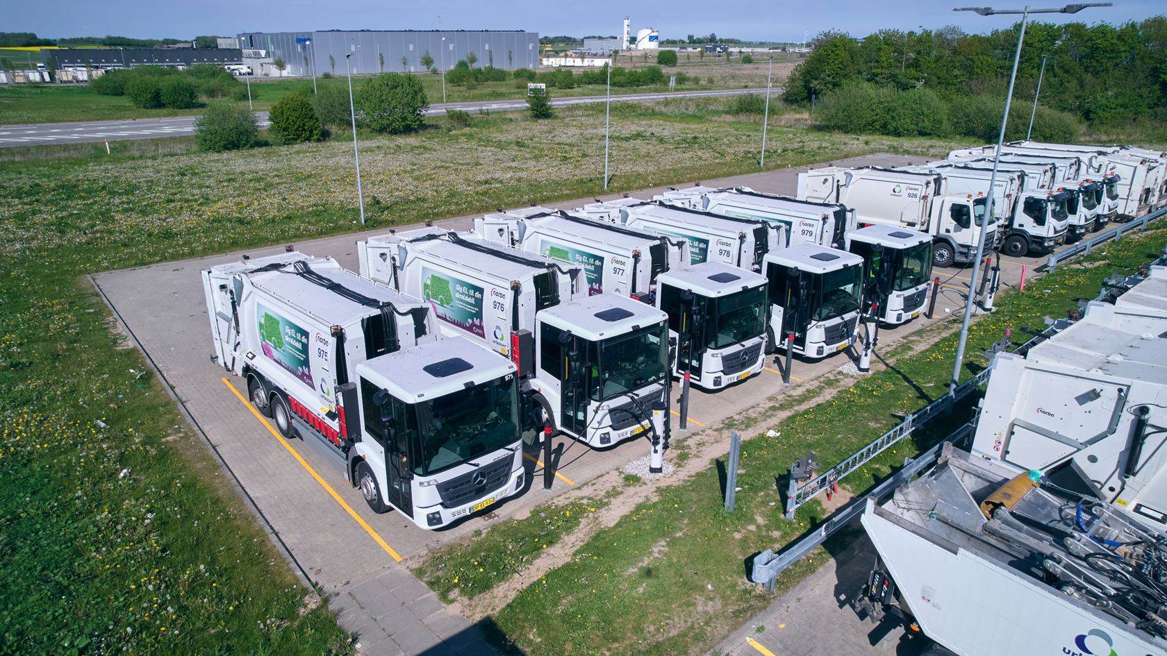 Luftaufnahme einer Flotte Mercedes-Benz eEconic Müllfahrzeuge an Ladestationen.