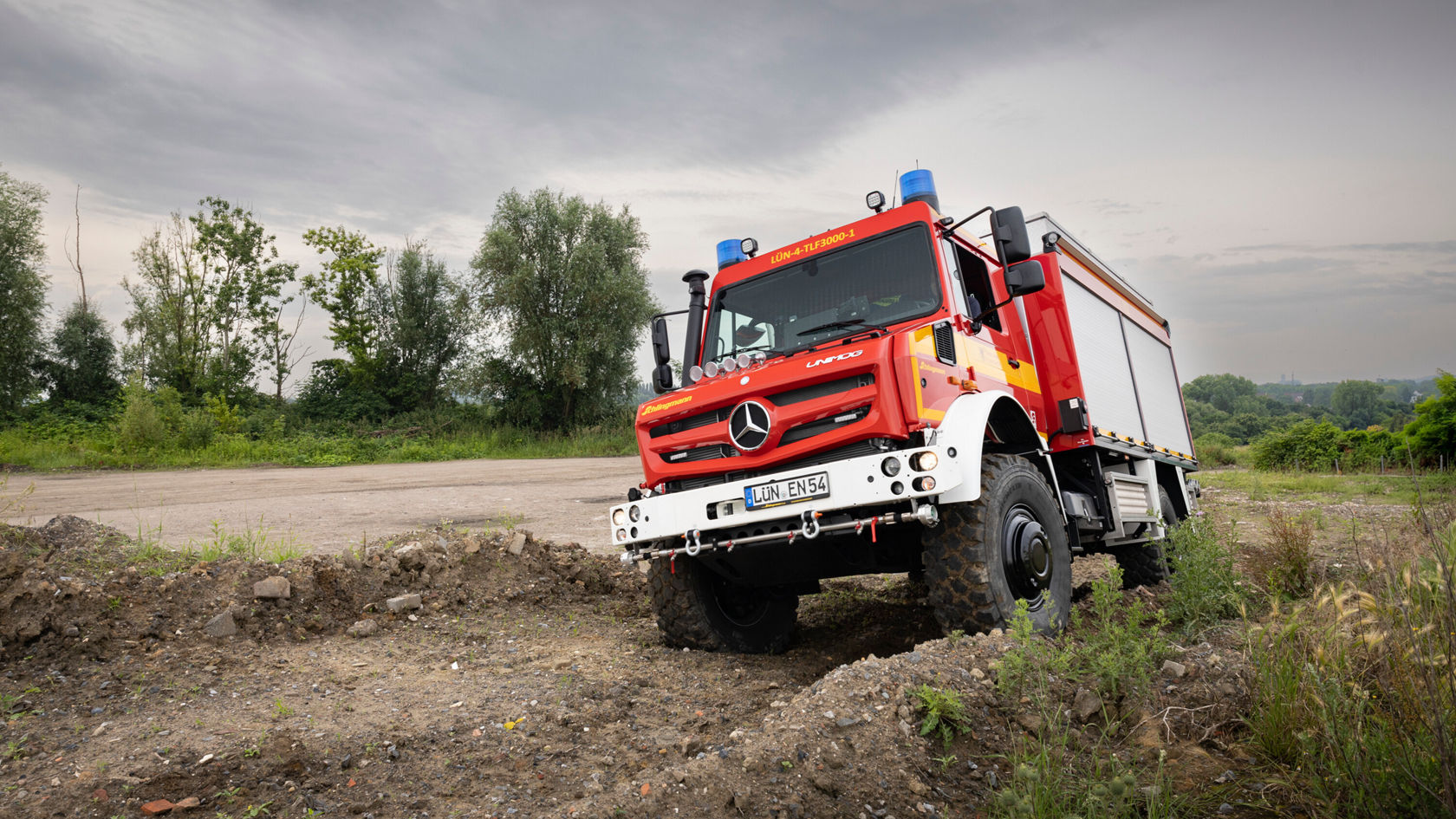 Ein roter Mercedes-Benz Unimog Feuerwehrwagen fährt auf unbefestigtem Terrain.