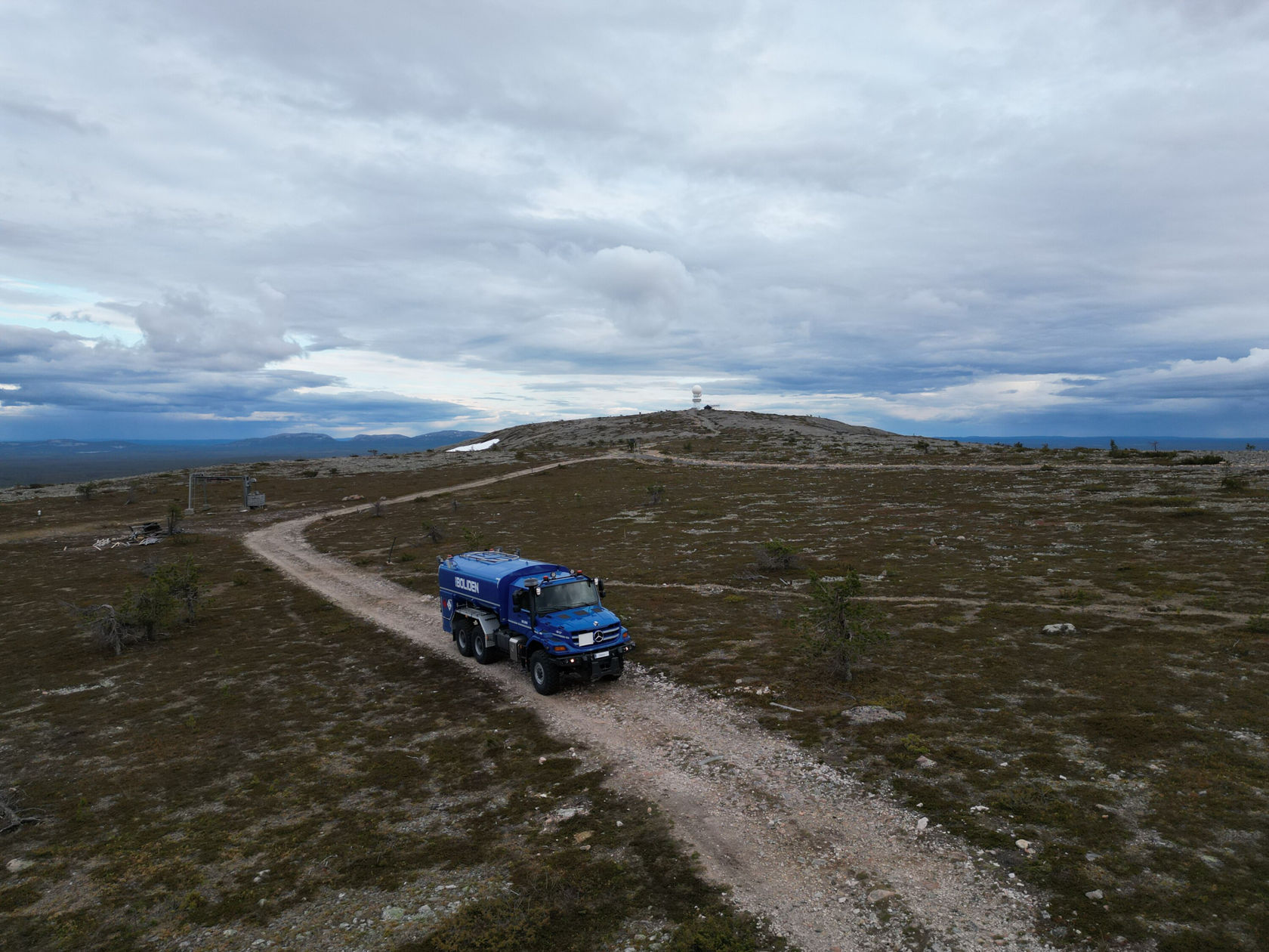 Ein blauer Zetros Tankwagen fährt auf einem schmalen, kurvenreichen Weg durch eine weitläufige, felsige Landschaft. 