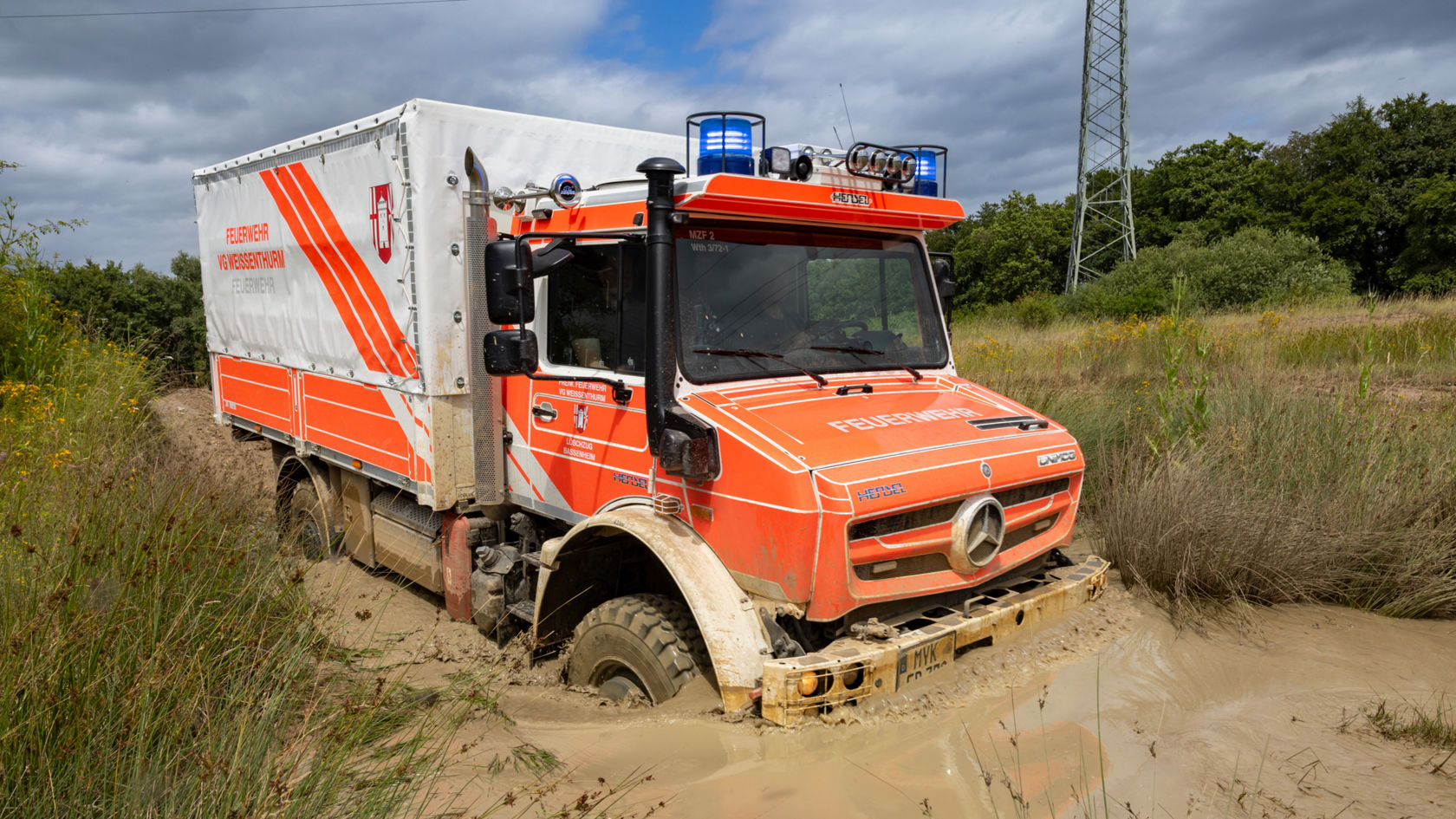 Un Unimog Mercedes‑Benz roule dans la boue.