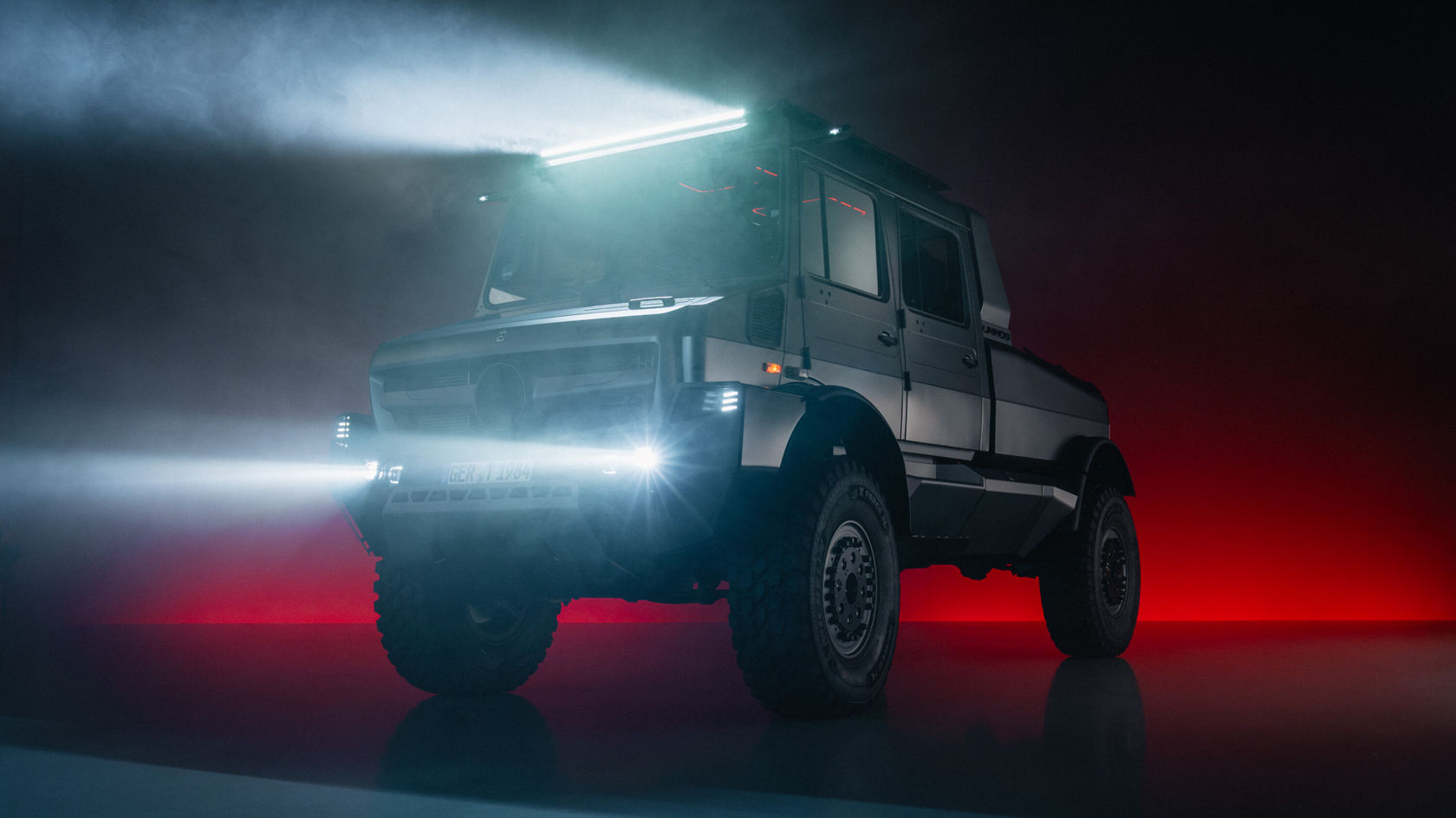 A black Mercedes-Benz Unimog with its headlight on, standing in a dimly lit room, surrounded by a misty atmosphere and red light accents.
