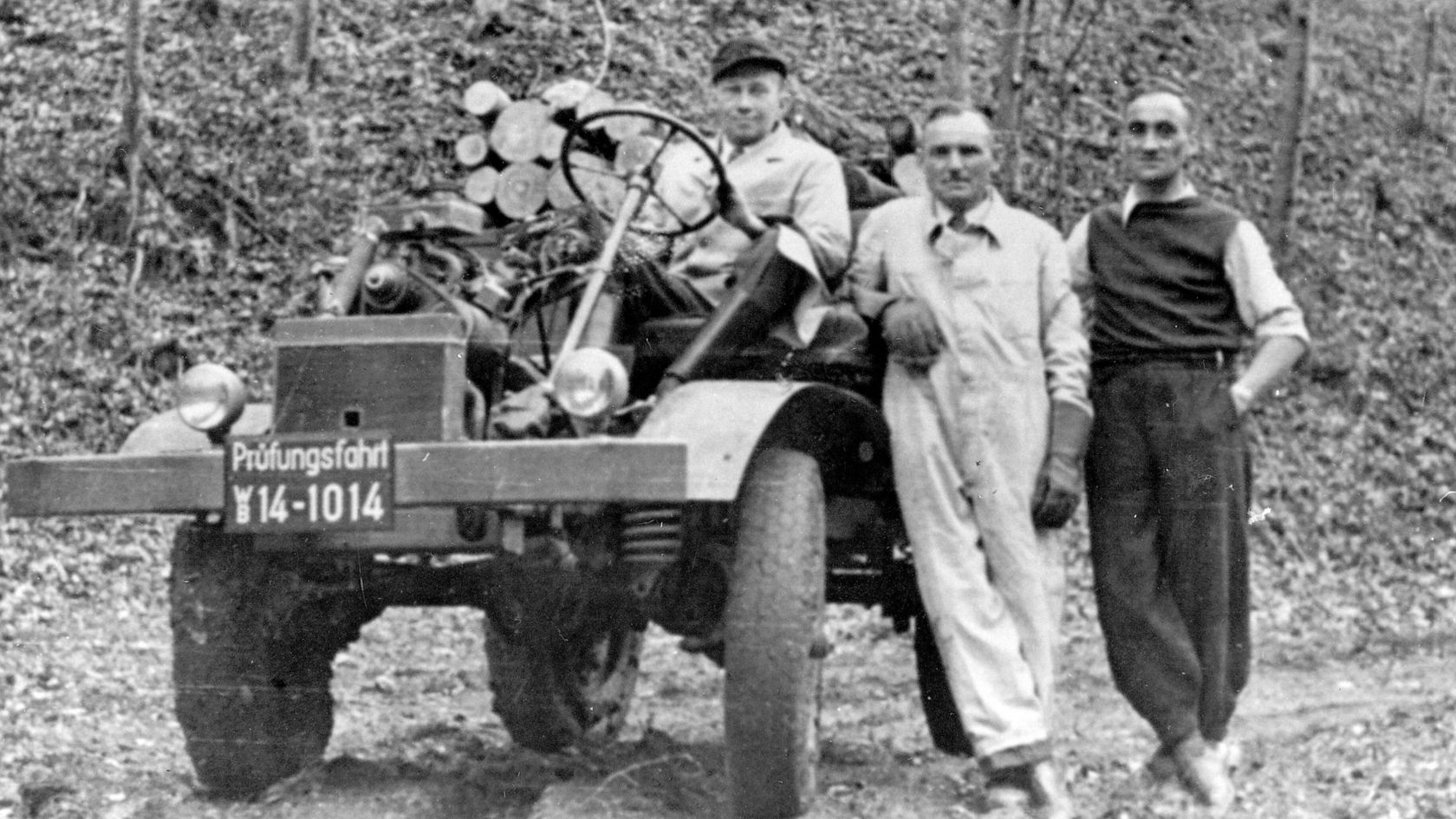 Drei Männer stehen neben einem Unimog von Mercedes-Benz, der mit technischem Equipment ausgestattet ist. Der Unimog hat das Kennzeichen "Prüfungsfahrt 14-1014".