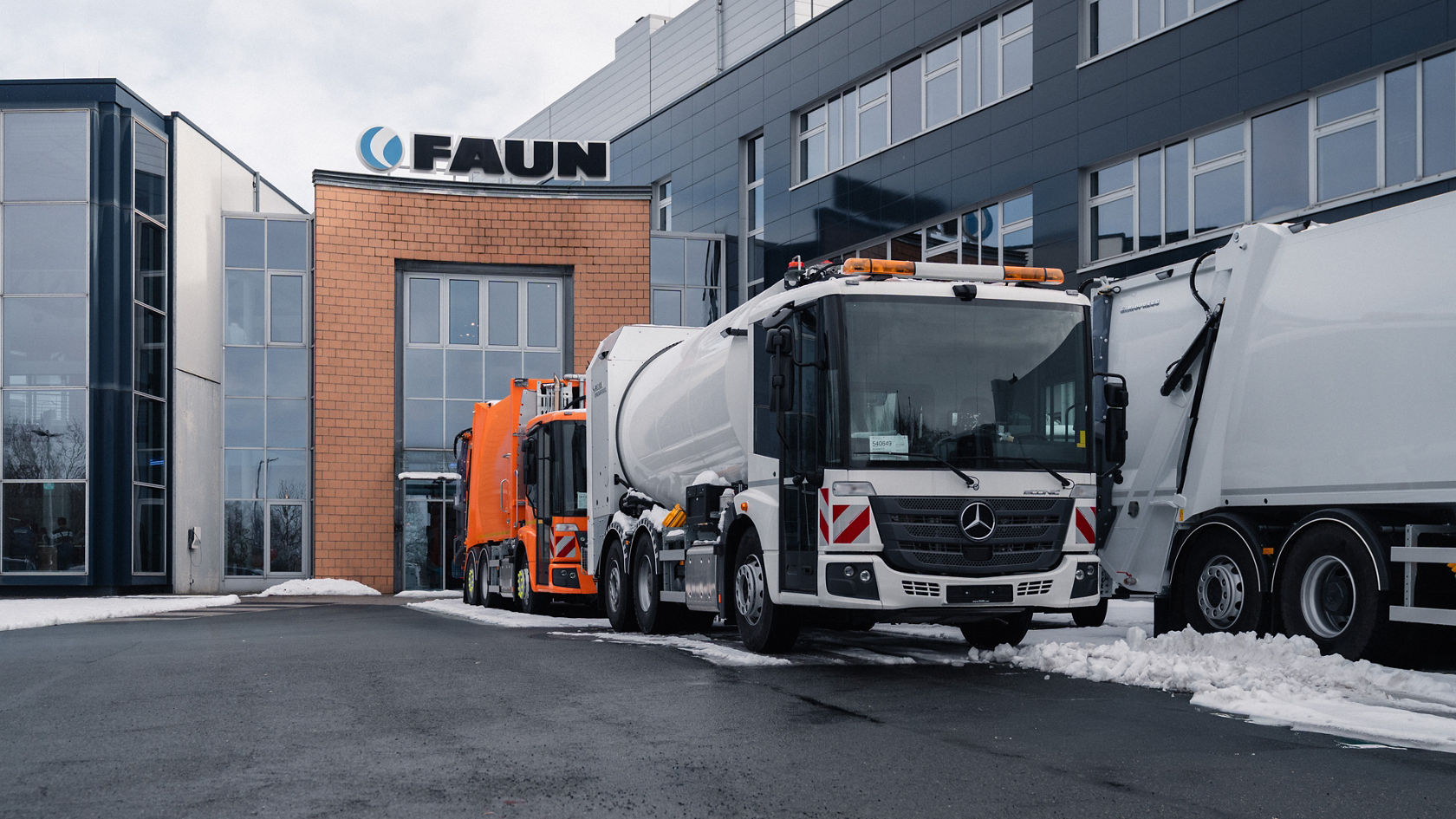 Zwei Mercedes-Benz Econic Müllfahrzeuge von FAUN stehen im Winter vor dem FAUN-Firmengebäude.