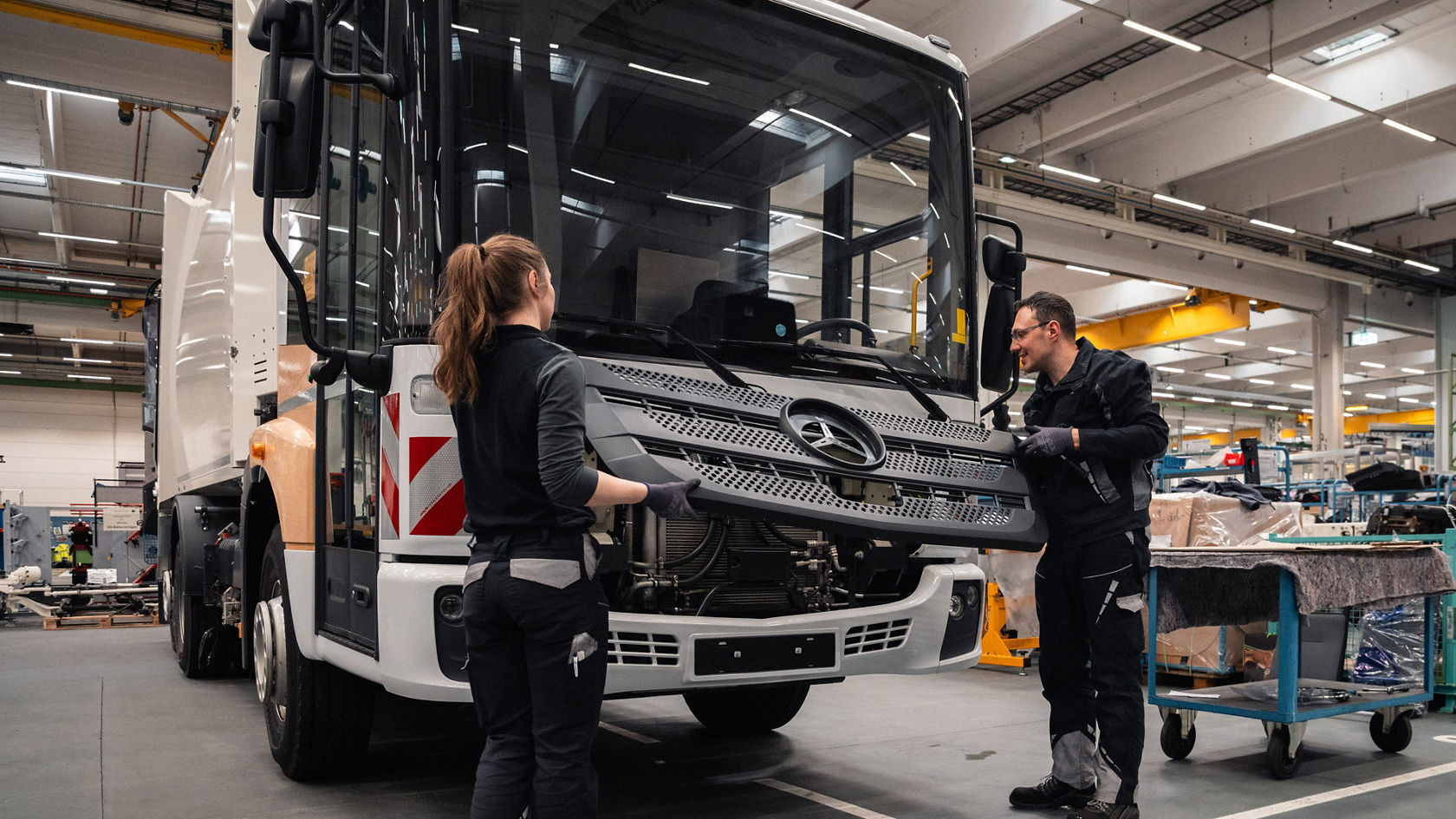 Zwei Mitarbeitende montieren den Kühlergrill an einem Mercedes-Benz Econic in der Fertigungshalle.