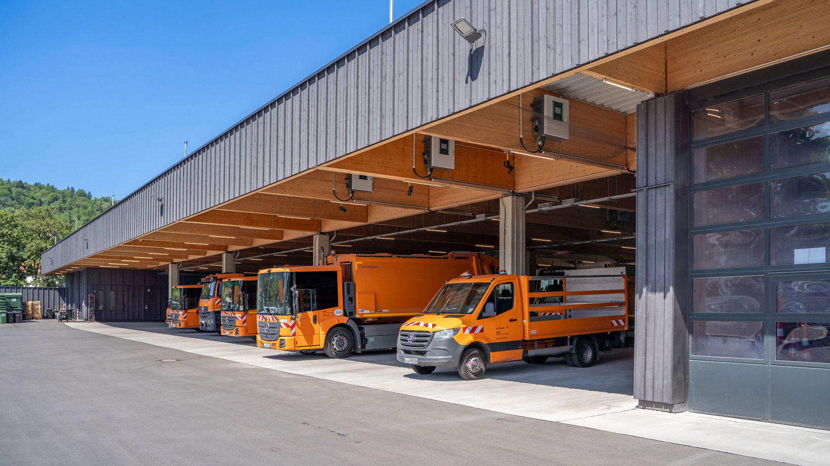 Orangefarbene Mercedes-Benz eEconic Abfallsammelfahrzeuge unter dem überdachten Vorplatz der neuen AWS-Betriebsstelle in Stuttgart-Wangen.