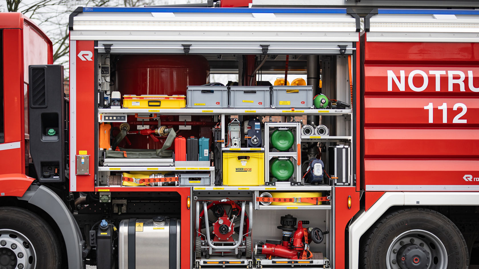 Le compartiment latéral d'un véhicule de pompiers montre différents équipements, tels que des tuyaux, des outils et du matériel de sécurité, rangés de façon ordonnée dans des compartiments.