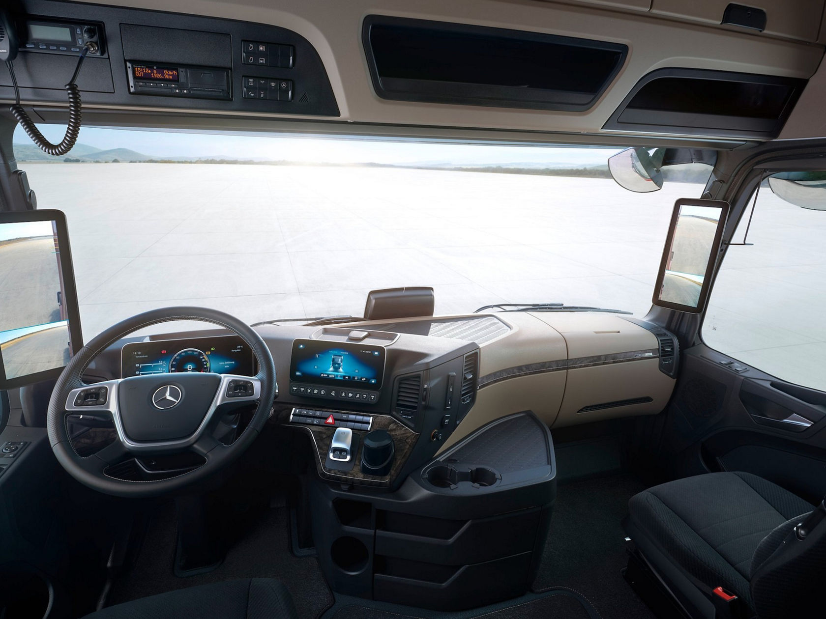 Das Innere der Fahrerkabine eines LKW. Man blickt auf das moderne Cockpit mit Lenkrad, digitalen Bildschirmen und der großen Frontscheibe.
