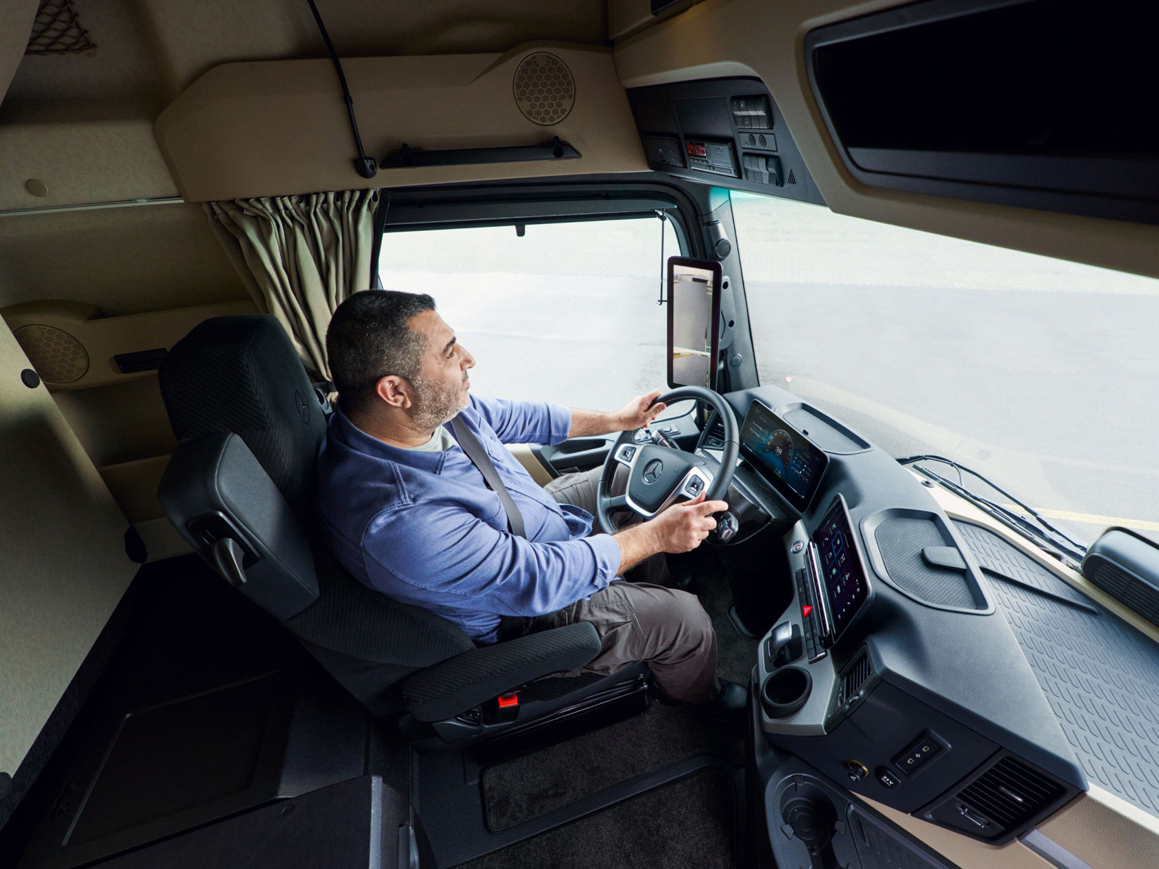 Ein Mann sitzt am Steuer in der Fahrerkabine eines Lkw und fährt. Die Aufnahme von oben zeigt ihn und das moderne Cockpit.