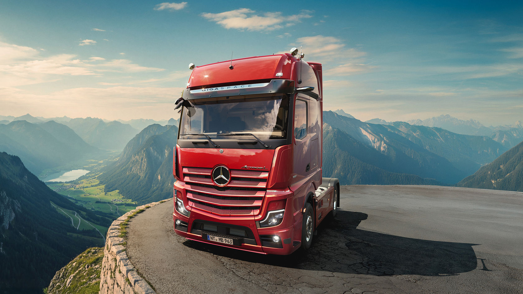 Ein roter Actros L steht an einer Straße am Rand einer deutschen Alpenvorlandschaft.