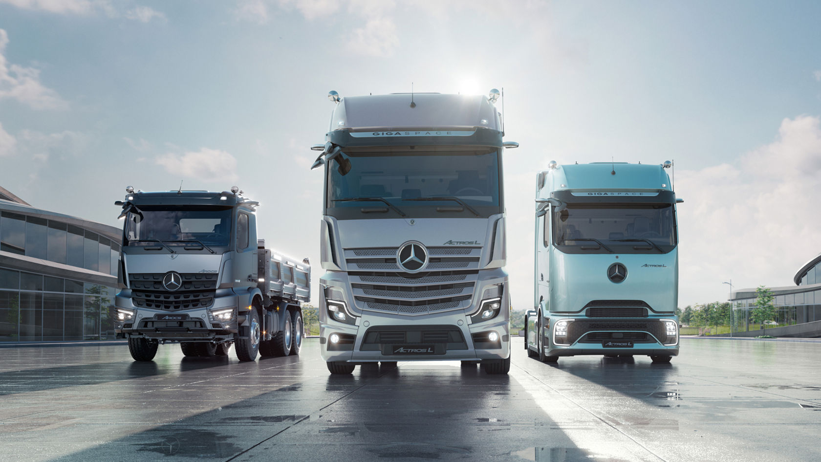 Drei verschiedene Mercedes-Benz Lkw-Modelle stehen nebeneinander auf nassem Asphalt. Im Hintergrund ist ein modernes Gebäude zu sehen.