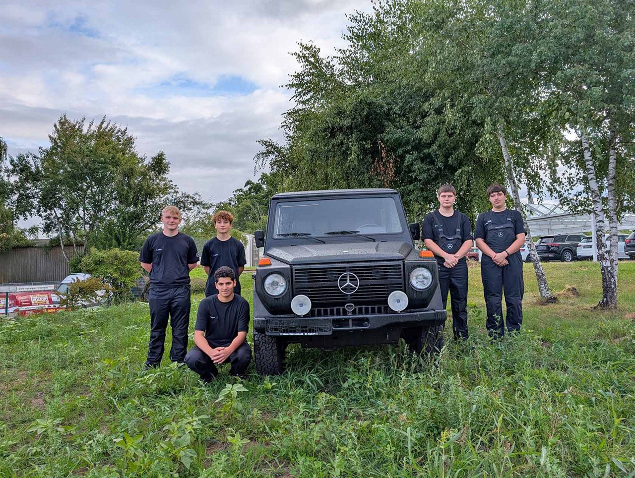 Fünf junge Menschen stehen auf einer grünen Wiese um ein Fahrzeug herum.