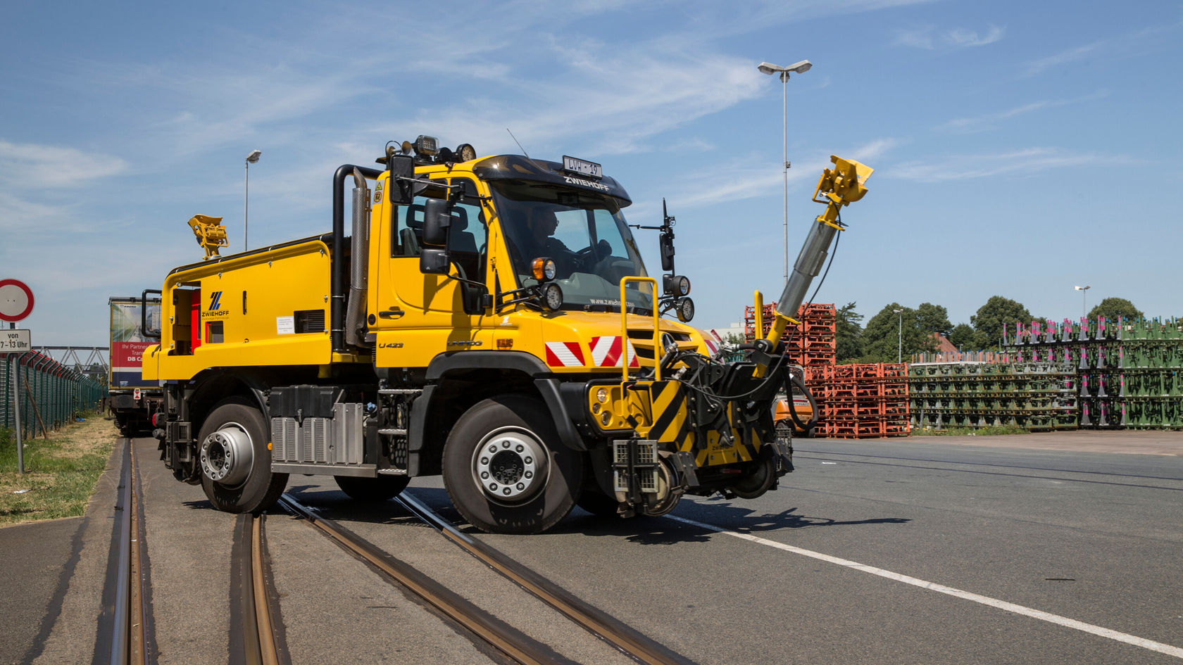 Ein gelber Unimog von Mercedes-Benz steht auf Schienen, ausgestattet mit einem Arbeitsarm und weiteren Werkzeugen, um infrastrukturelle Aufgaben durchzuführen.