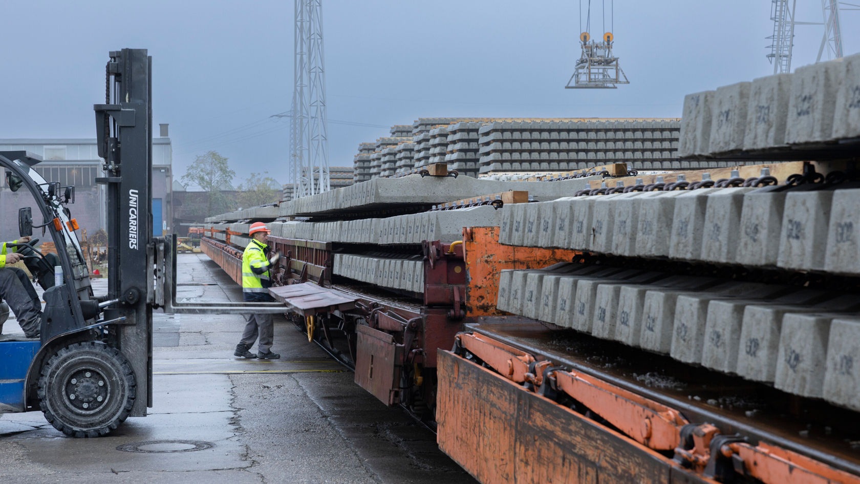 Ein Gabelstapler hebt Betonplatten von einem Waggon ab. Ein Arbeiter in Warnweste und Schutzhelm steht neben dem Waggon.