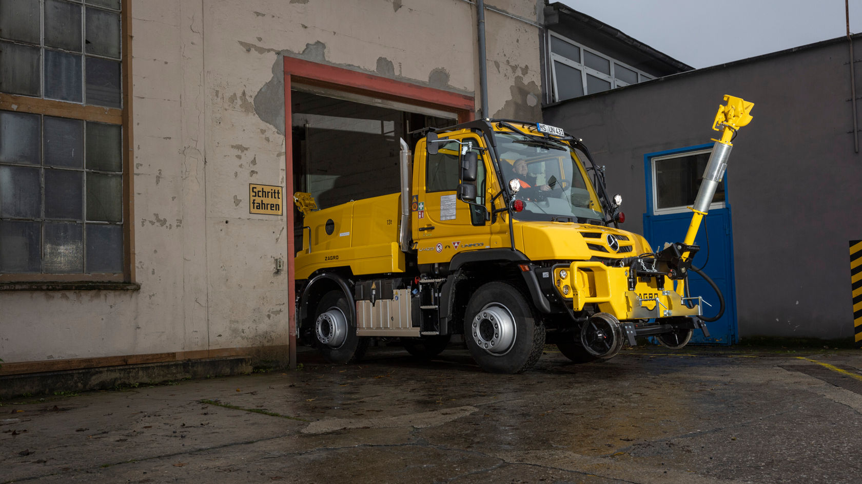 Ein gelber Zweiwege Unimog steht vor einem Gebäude.