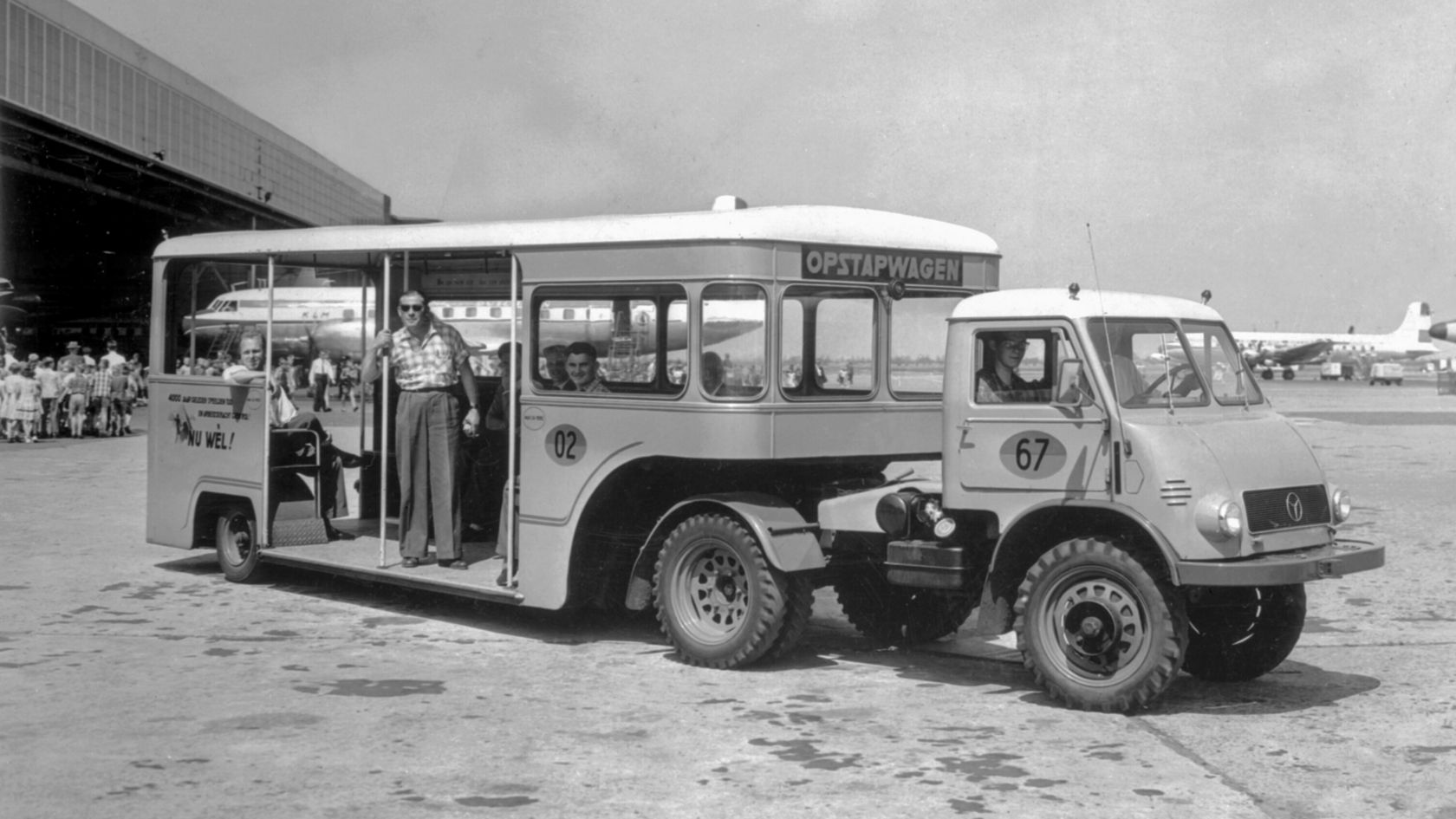 Ein Mercedes-Benz Unimog als Bus, der als Ortswagen genutzt wird. Das Fahrzeug steht auf einem Flughafengelände, umgeben von Menschen.