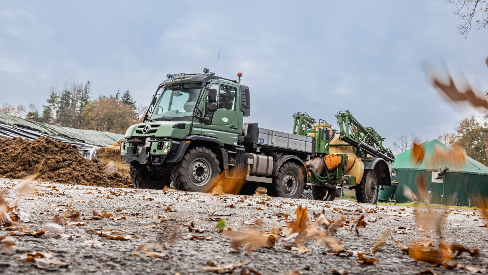 A green Unimog stands on a farm. It is equipped with a field sprayer.