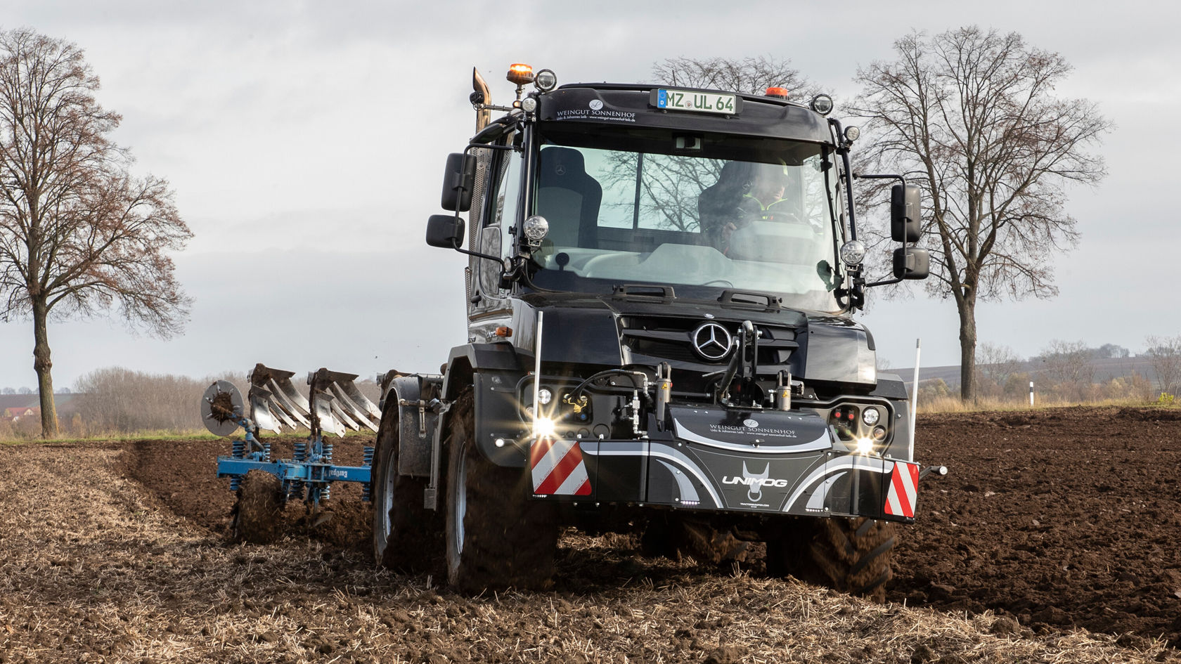 Un tracteur Mercedes-Benz laboure un champ. La machine présente un aspect moderne et travaille efficacement avec une charrue dans le sol. L'image évoque une activité agricole.