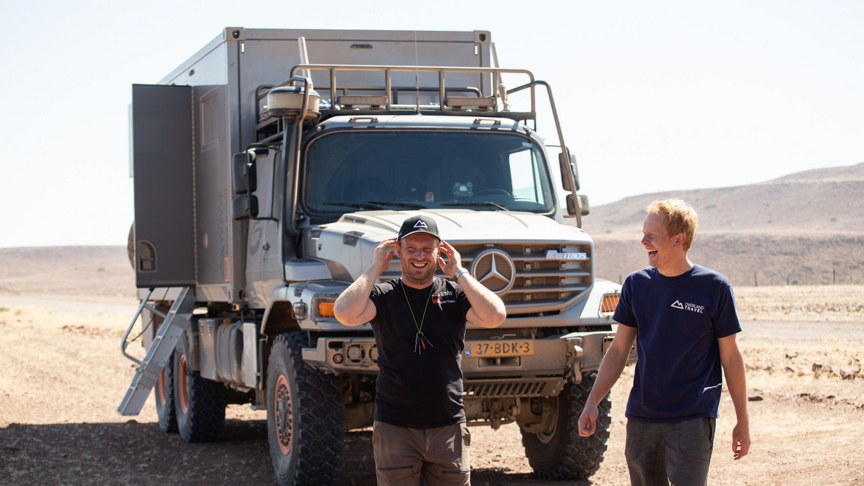 Zwei Personen stehen neben einem Mercedes-Benz Zetros in einer Wüste.