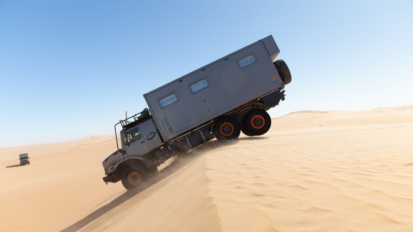 Ein Mercedes-Benz Zetros fährt in der Wüste einen Sandhügel hinunter.