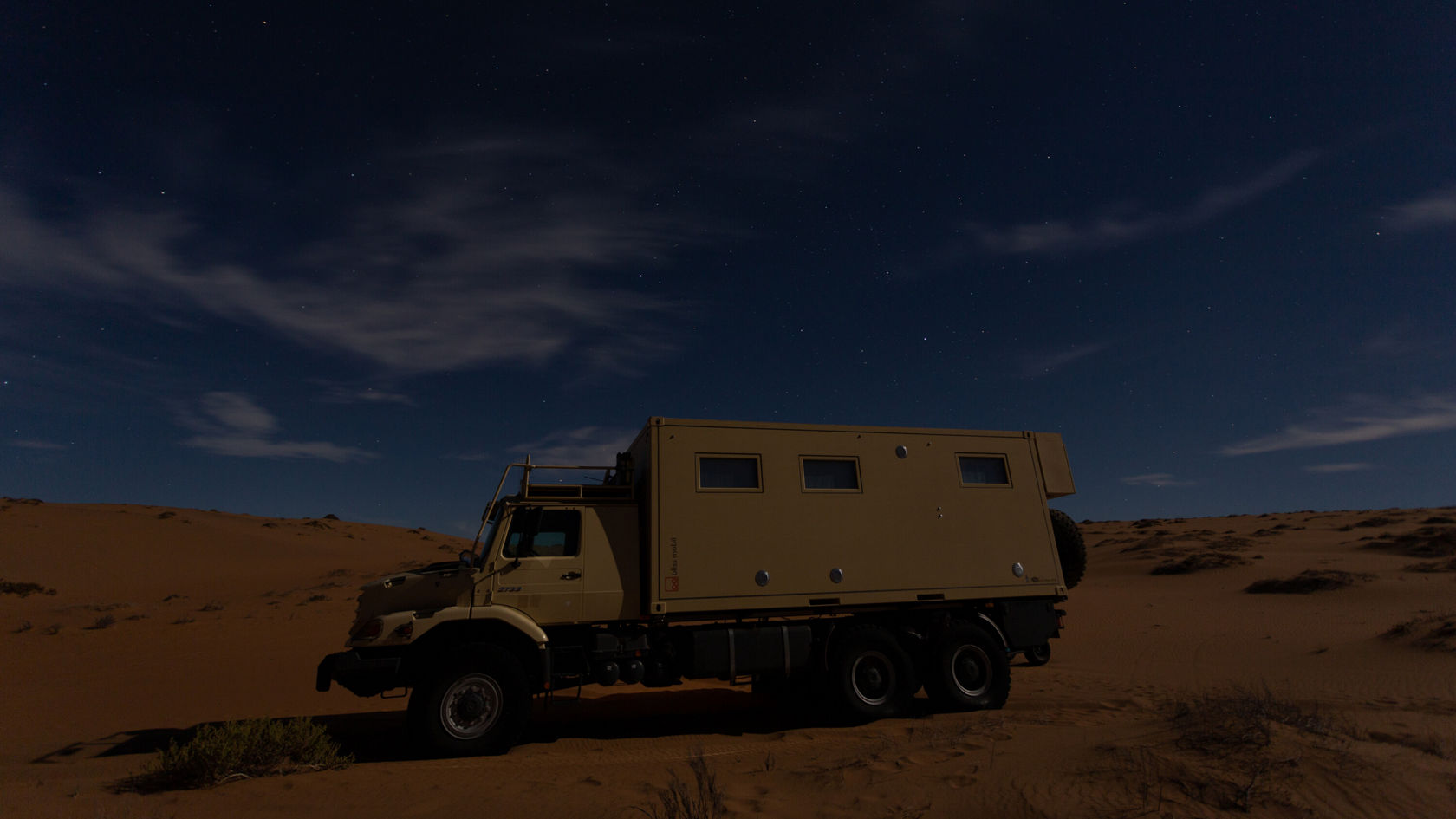 Ein Mercedes-Benz Zetros steht in einer Wüste bei Nacht, umgeben von Sanddünen und einem klaren Sternenhimmel.