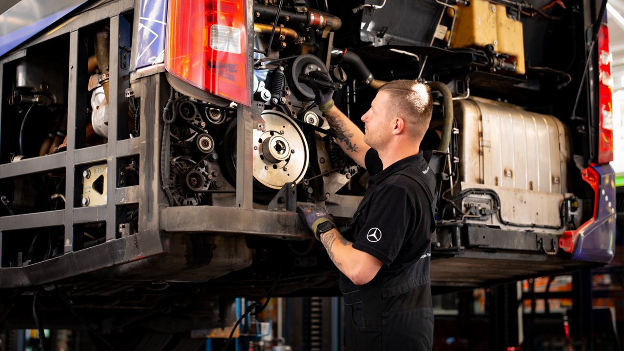 Ein Mechaniker steht vor der geöffneten Motorhaube eines Busses um diesen zu reparieren