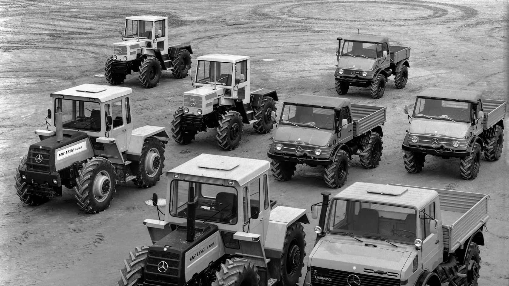 Several Mercedes-Benz Unimog vehicles are standing on soft ground, with two models in the foreground particularly highlighted.
