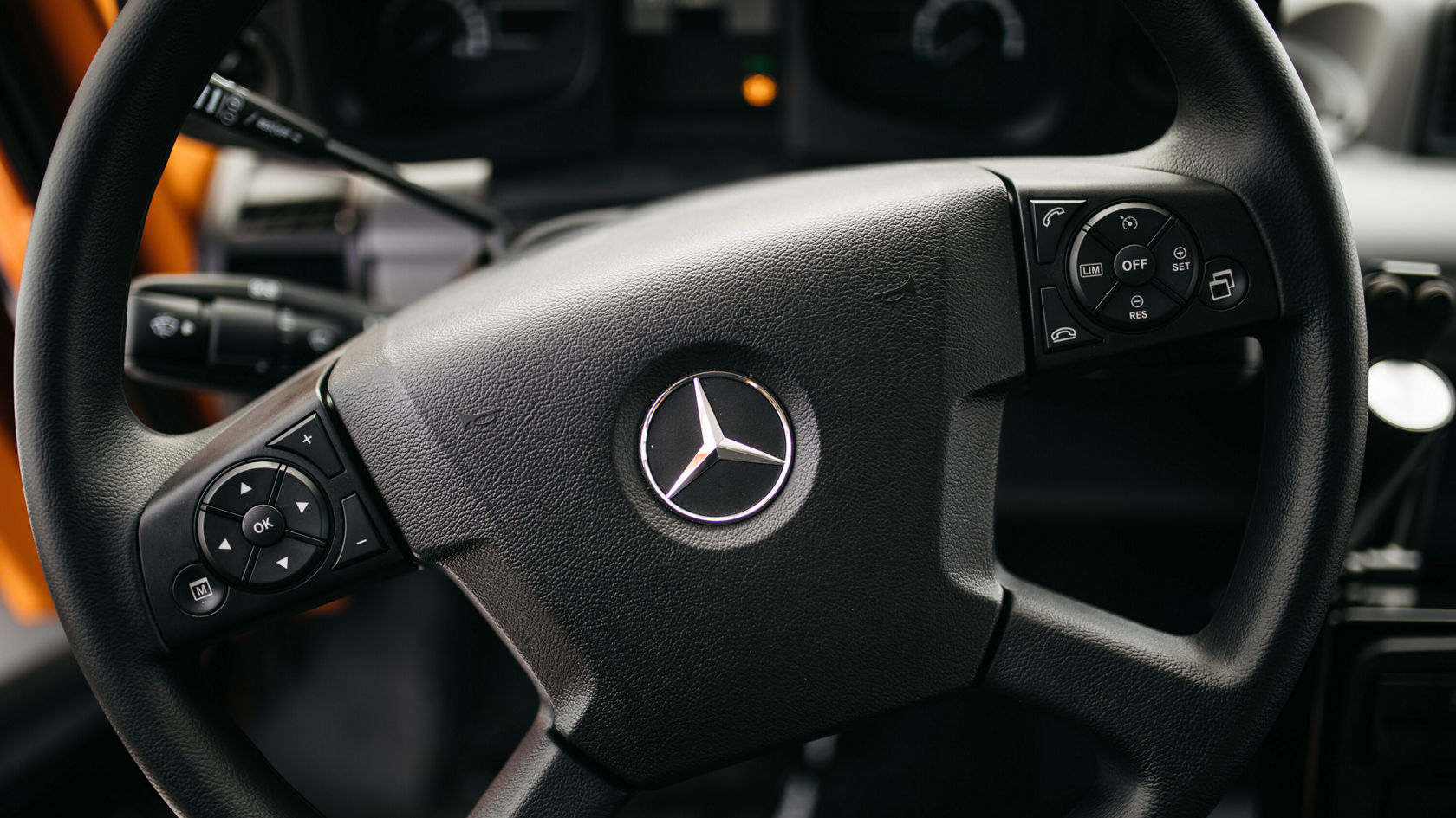 The steering wheel of a Mercedes-Benz Unimog with controls for functions such as cruise control and audio, embedded in a modern dashboard.