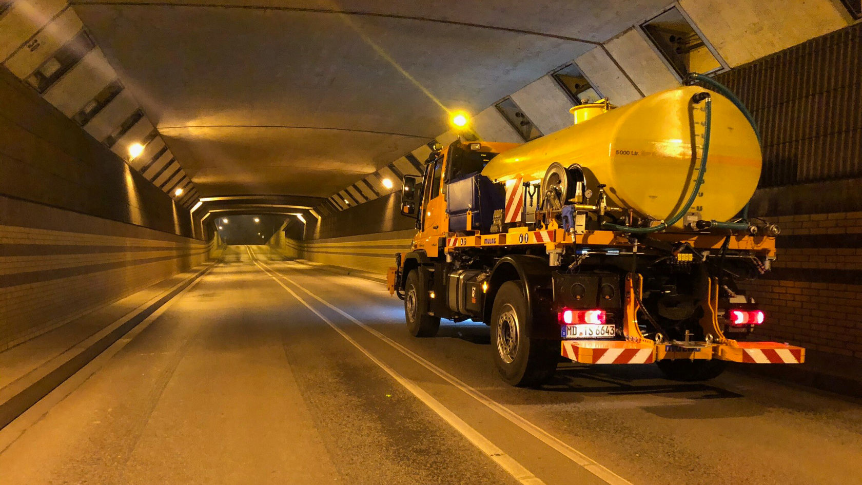 Een Mercedes-Benz Unimog staat in een tunnel op een lege rijbaan. De Unimog is uitgerust met een grote, ronde watertank.