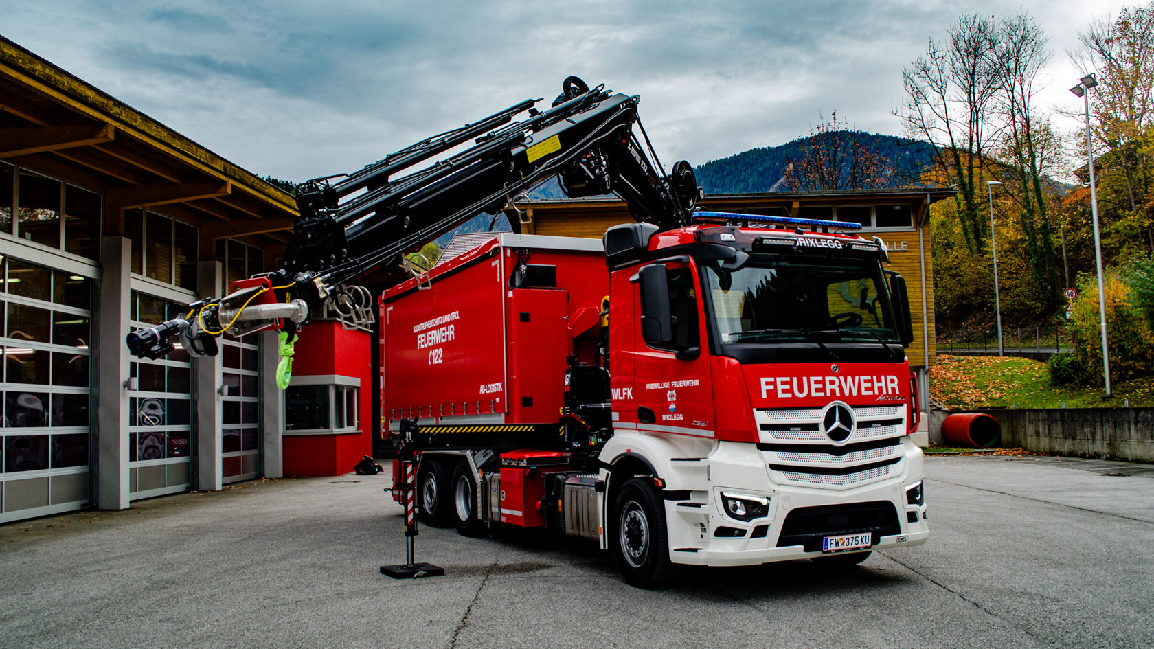 A red fire truck with a large boom stands in front of a fire station.