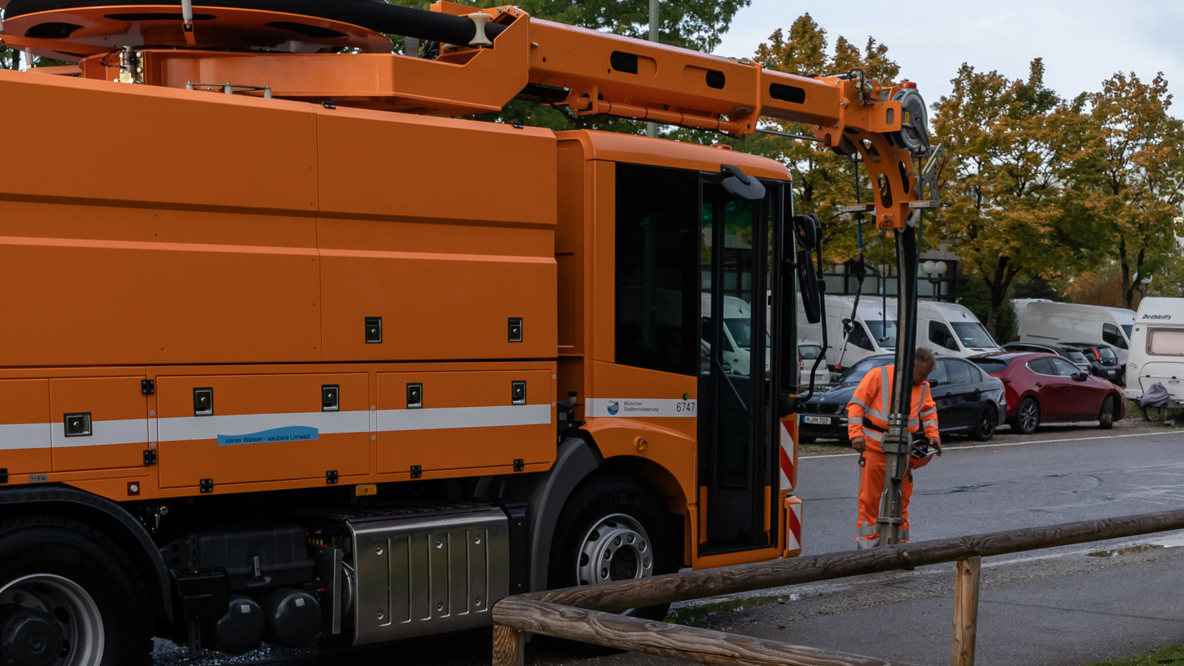 Ein orangefarbener Mercedes-Benz Econic-Lkw steht an einer Straßenkante, während ein Arbeiter in orangefarbener Sicherheitskleidung ihn bedient.