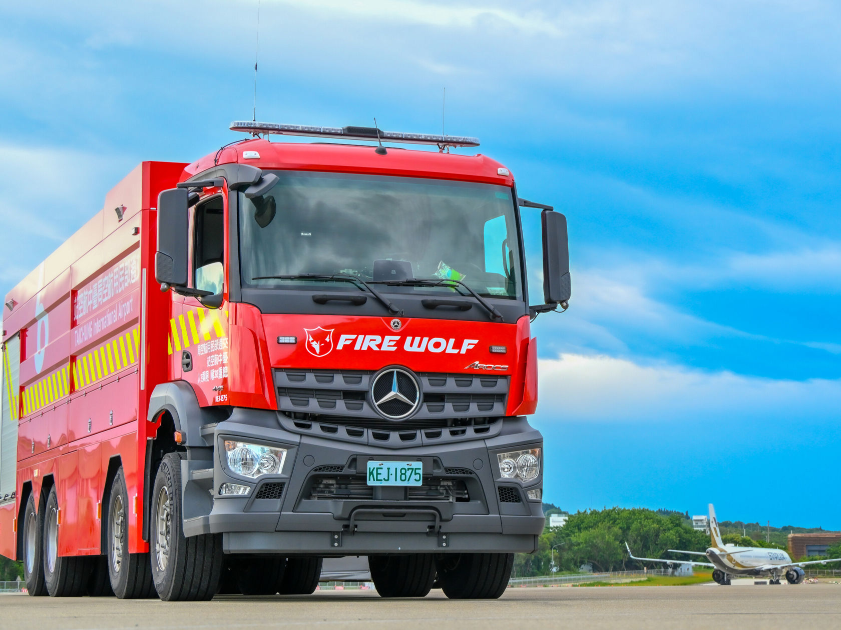 Ein roter Feuerwehrtruck mit der Aufschrift "FIRE WOLF" steht auf einer Flugplatzfläche. Der Truck hat vier Achsen.