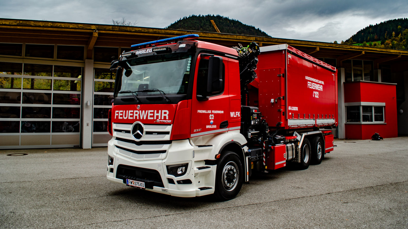 A fire-fighting vehicle with red paint stands in front of a fire station.