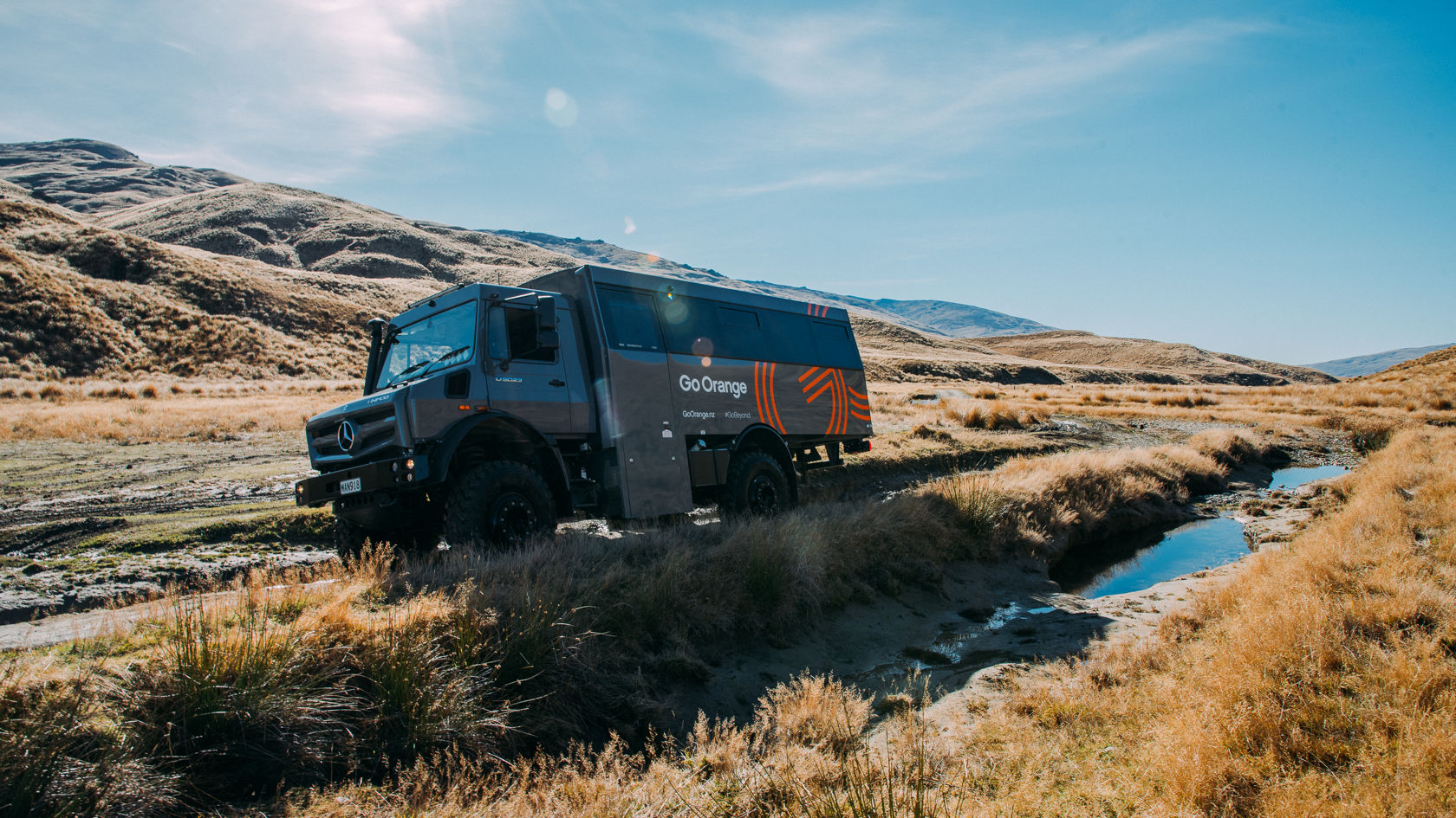 Ein Mercedes-Benz Geländewagen steht am Ufer eines schmalen Baches, umgeben von grasbewachsenen Hügeln und sanften Landschaften, ideal für Abenteuer und Offroad-Erlebnisse.