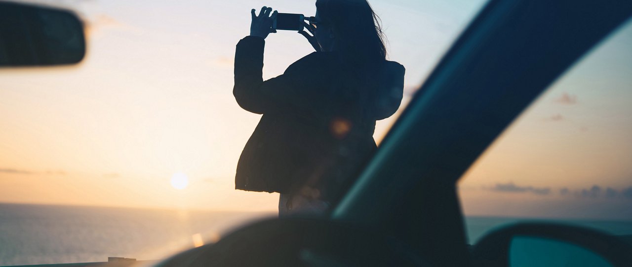 Frau am Meer mit Fahrzeug, fotografiert mit Handy
