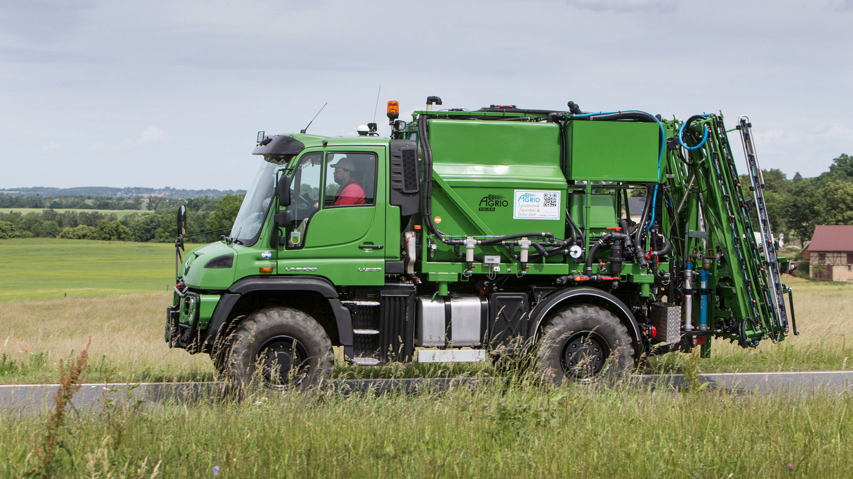 A green Unimog with an agricultural body is driving on a road.