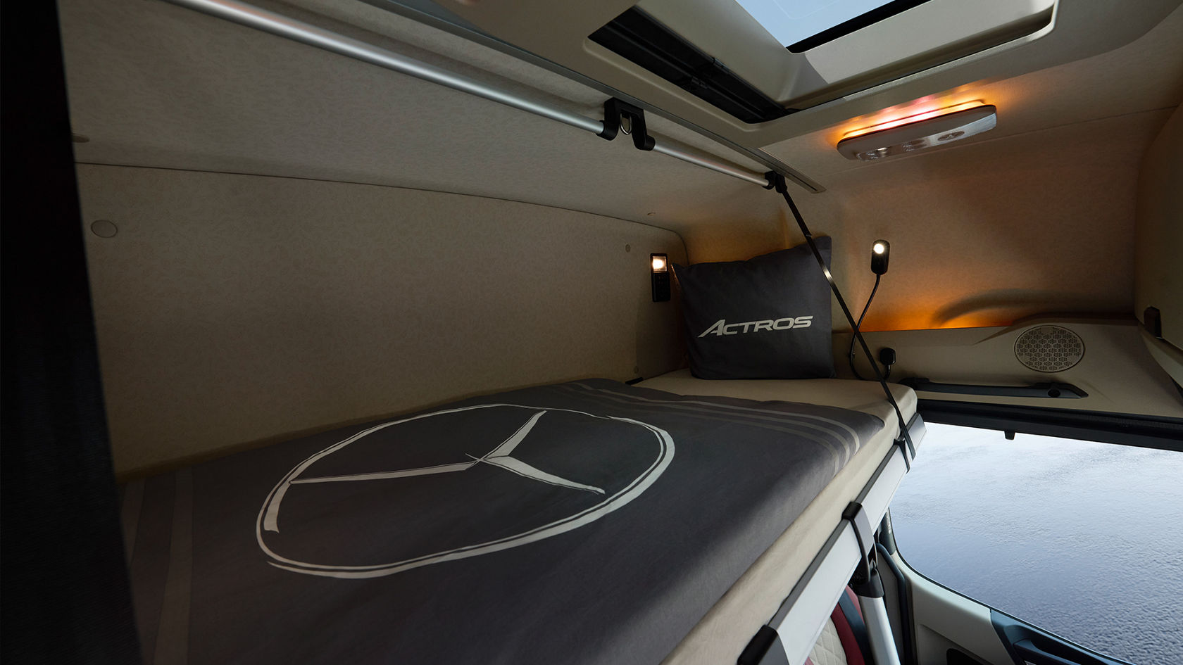 駕駛艙上層睡眠區的內部畫面：床鋪鋪著灰色被罩，並飾有白色 Mercedes-Benz 標誌，配有相襯的 Actros 枕頭、閱讀燈，並可看到天窗。