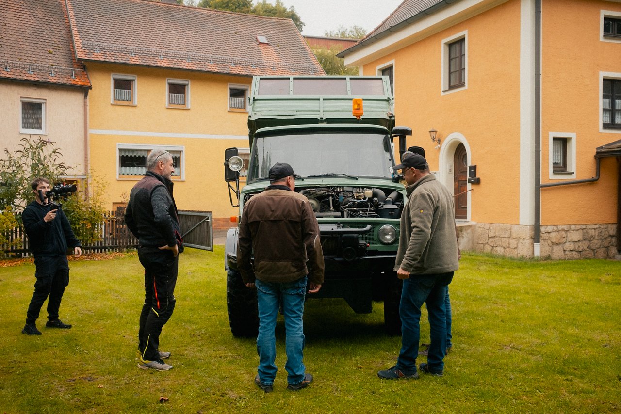 Drei Personen stehen vor einem historischen Unimog