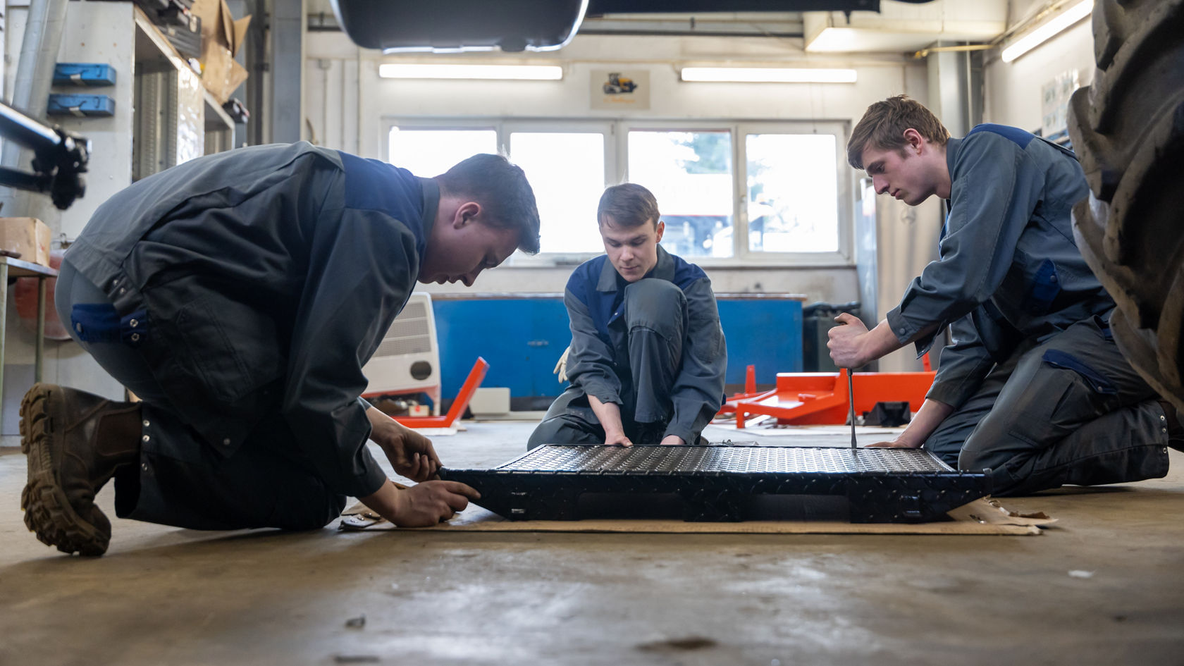 Drei Mechaniker arbeiten gemeinsam an einer großen Montagplatte im Werkstattbereich, ausgerüstet mit Werkzeugen und in Arbeitskleidung. Sie konzentrieren sich auf die präzise Montage.