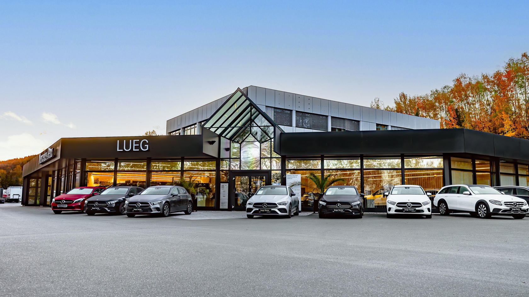 Autohaus Aue, Große Glasfront, schwarzes Dach, LUEG Schild links, mehrere Fahrzeuge vor dem Autohaus