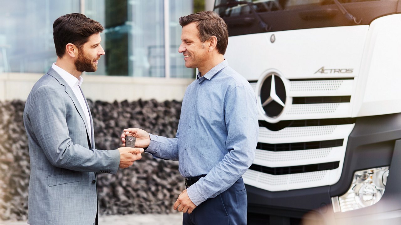 Een verkoper van Mercedes-Benz Trucks geeft een sleutel aan een man die net een truck heeft gekocht. Op de achtergrond staat de truck.
