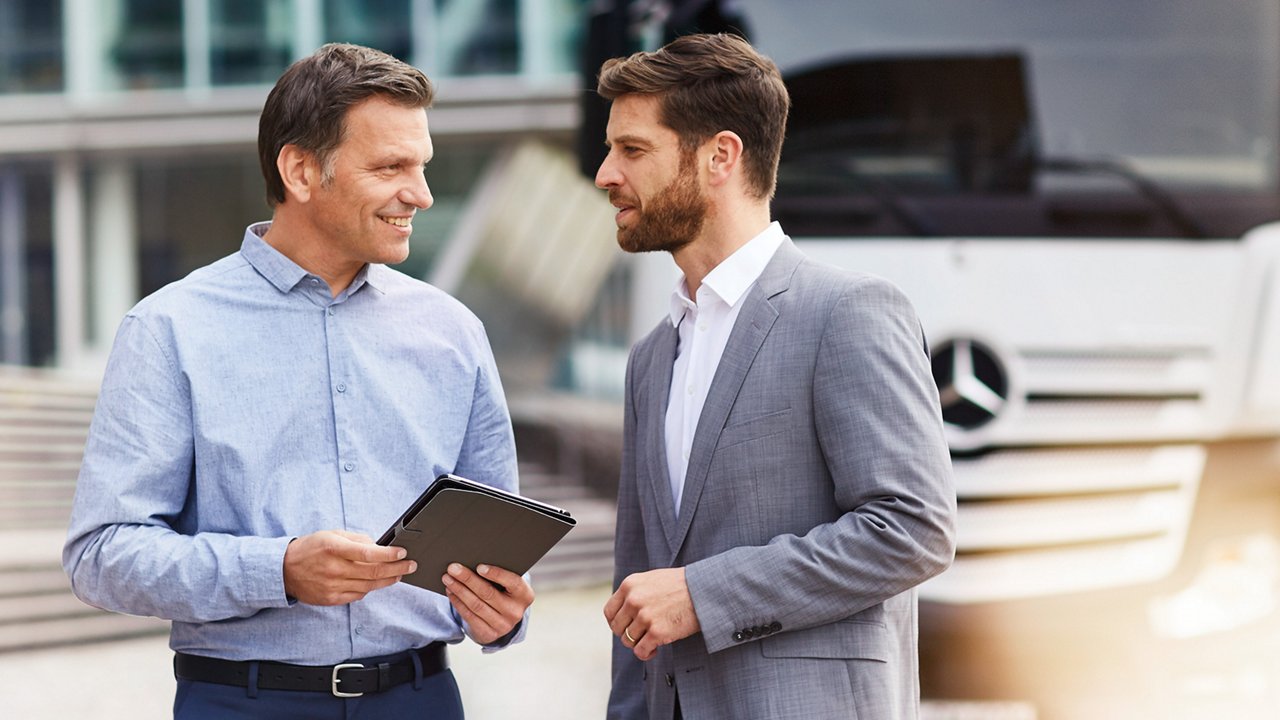 2 mannen staan voor een witte Mercedes-Benz Truck. Ze bespreken de verkoop van de truck.