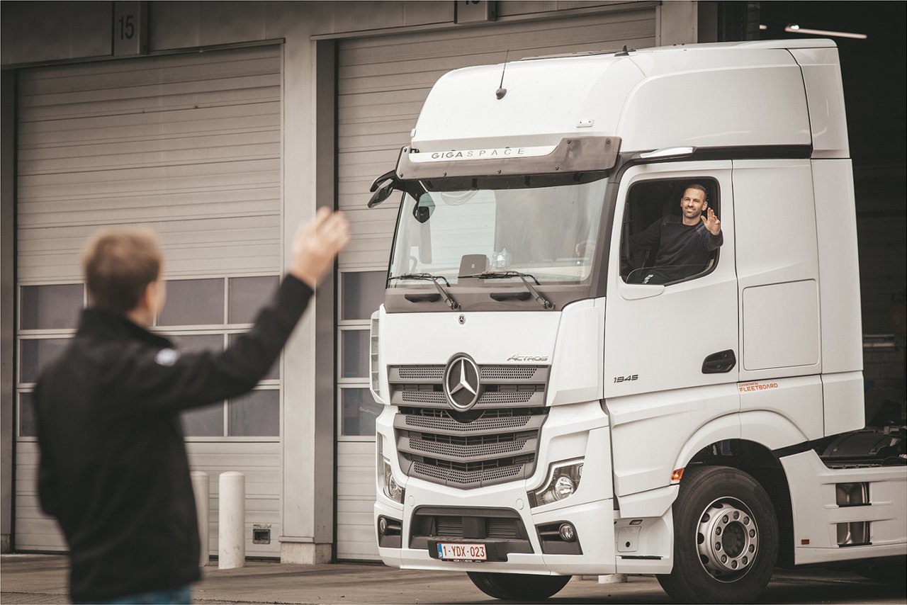 Witte Actros met inzittende man zwaait naar man die buiten staat. 