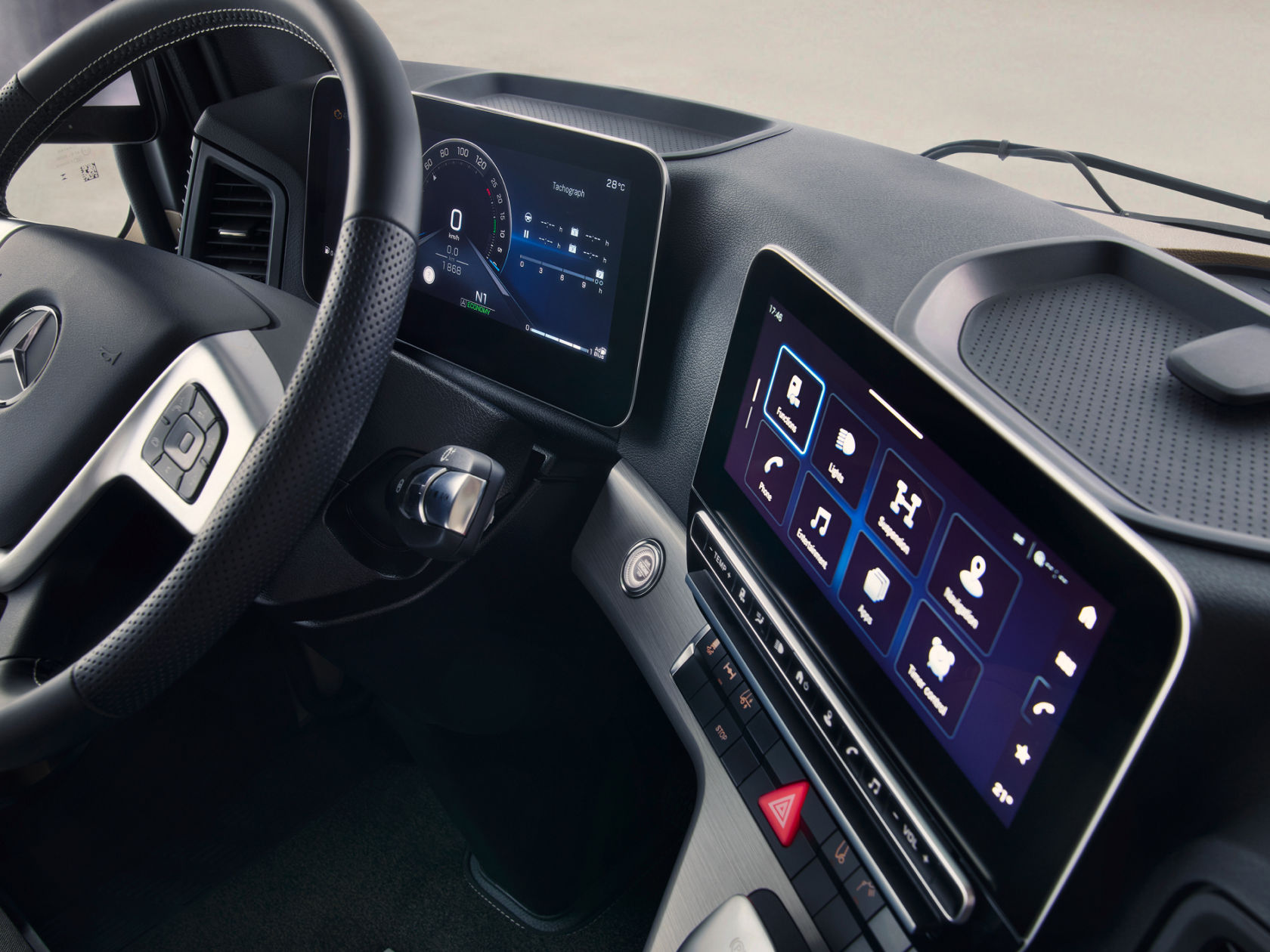 L'image montre l'intérieur moderne d'un camion Mercedes-Benz, l'accent étant mis sur le volant et les écrans numériques. On voit un combiné d'instruments numérique derrière le volant et un grand écran tactile dans la console centrale qui affiche différentes fonctions telles que la navigation et le divertissement.