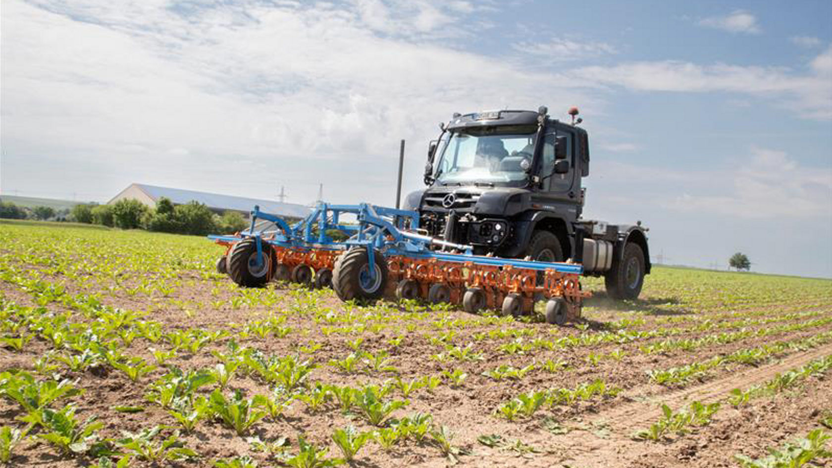 Grüner Unimog mit Pflug vorne.